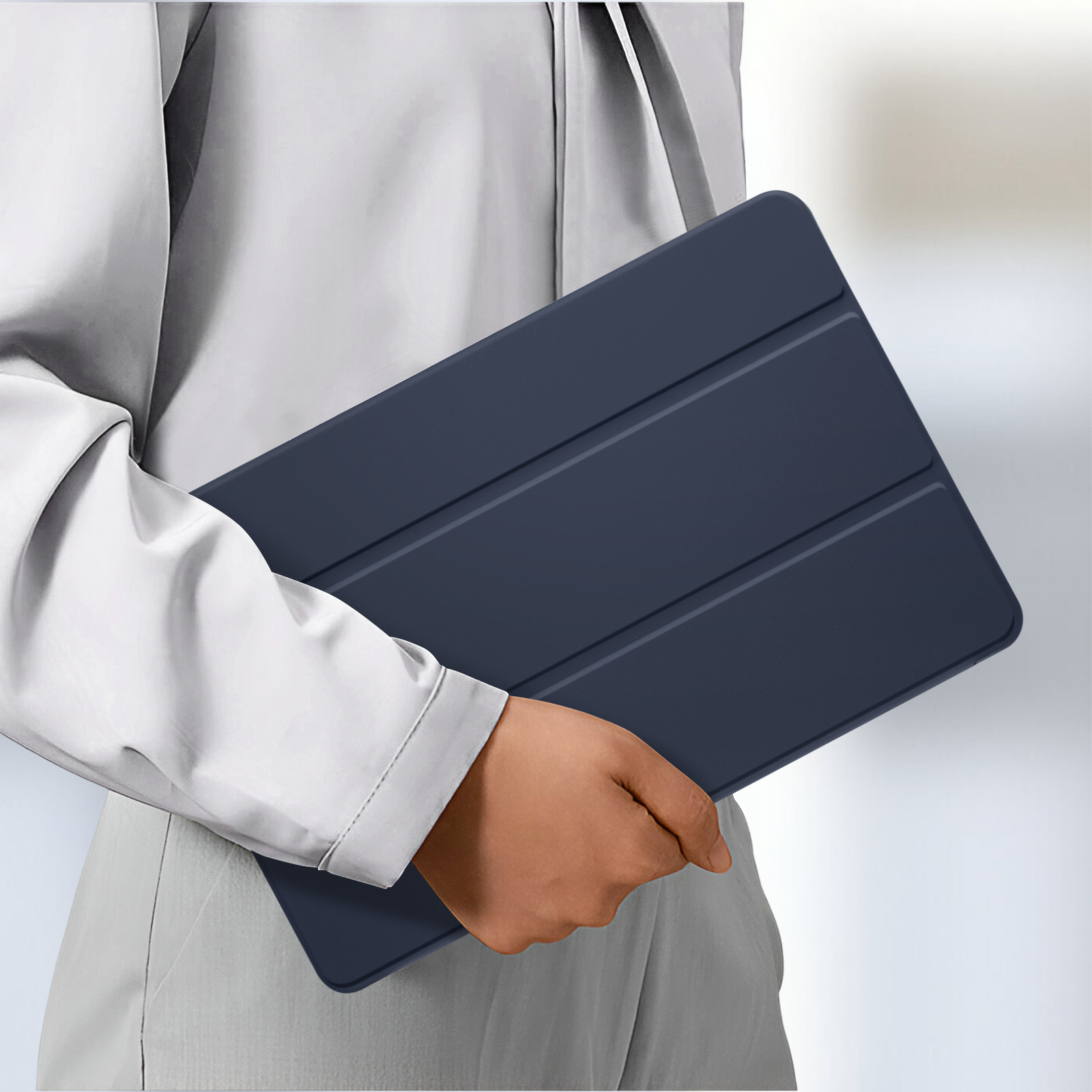 Una persona che tiene una custodia per tablet blu scuro chiusa su uno sfondo grigio chiaro.
