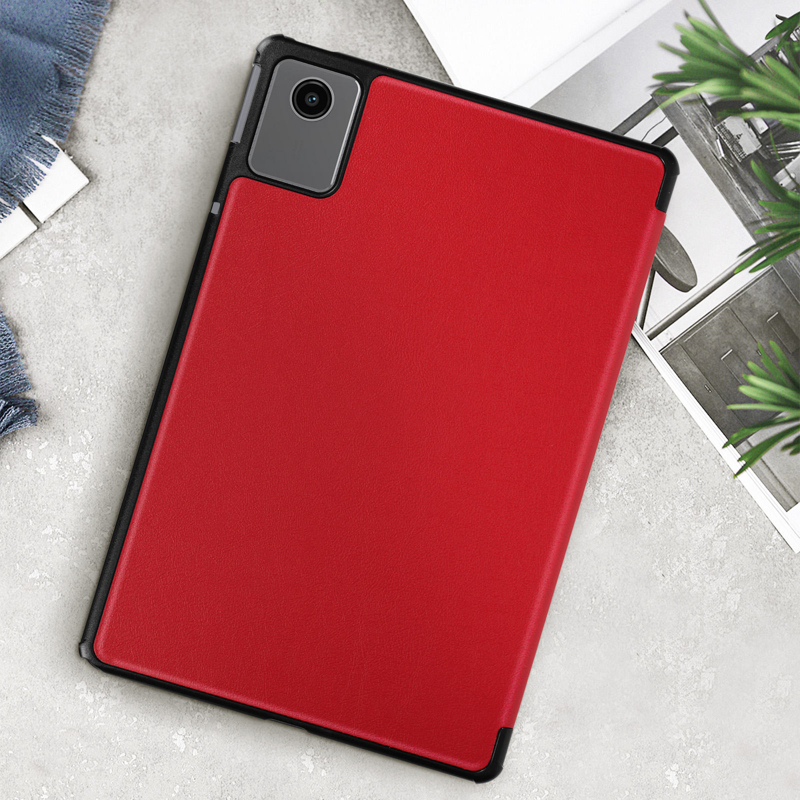 Custodia rossa per tablet su un tavolo con rivista, fotocamera e penna.