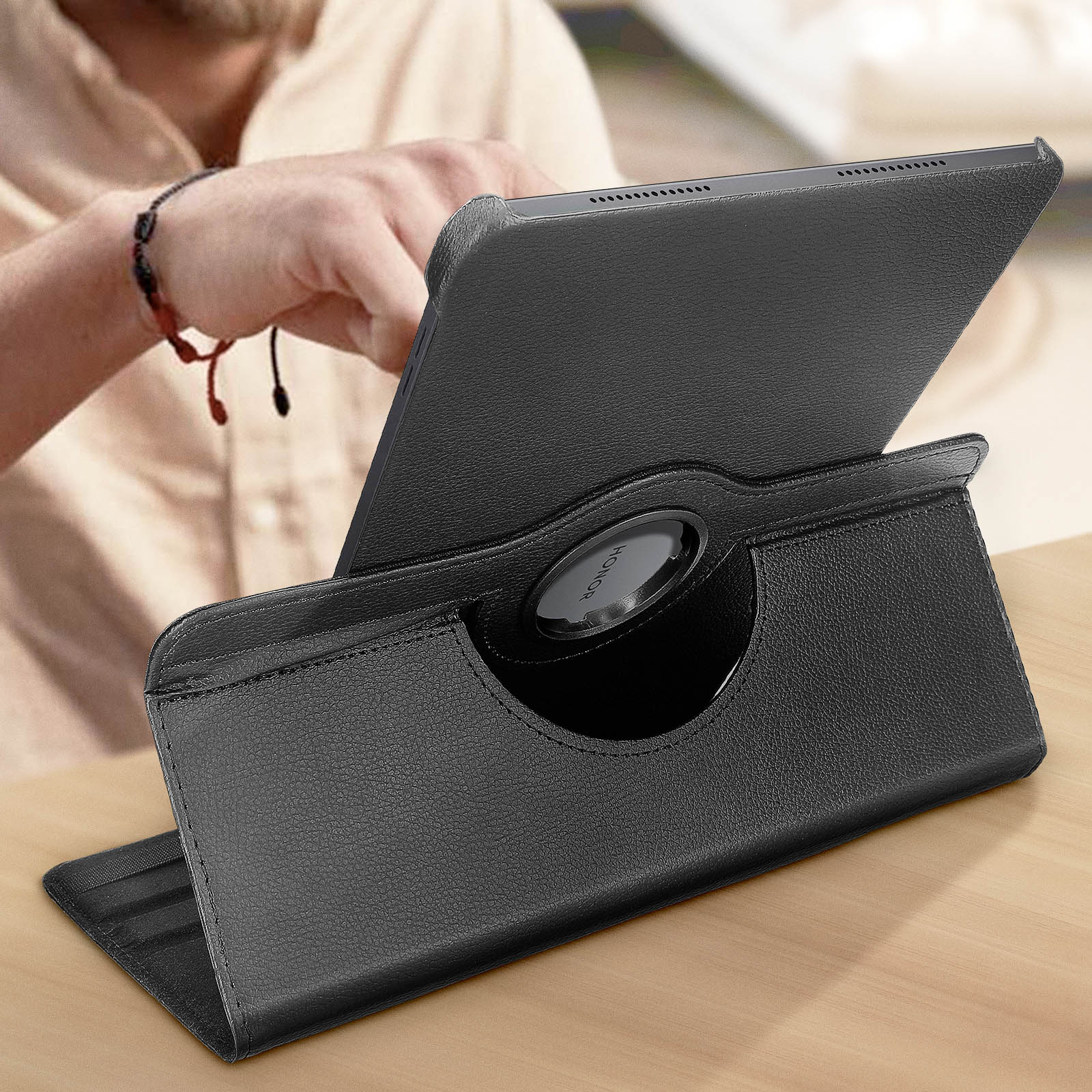 Tablet nero in una custodia di pelle nera, su un tavolo di legno. Una persona lo tiene.