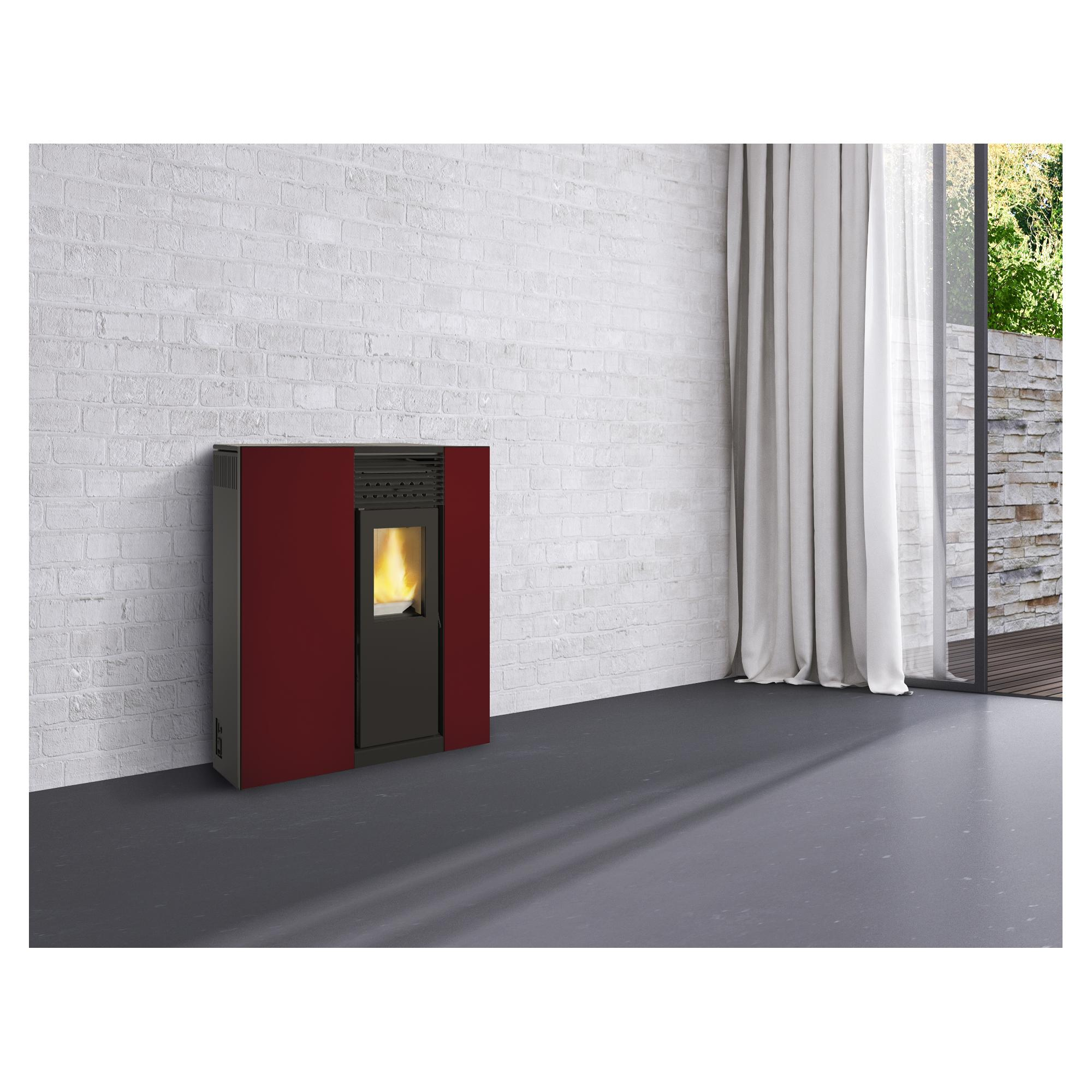 Una estufa de pellets roja, negra y gris contra una pared de ladrillo blanco con una ventana.