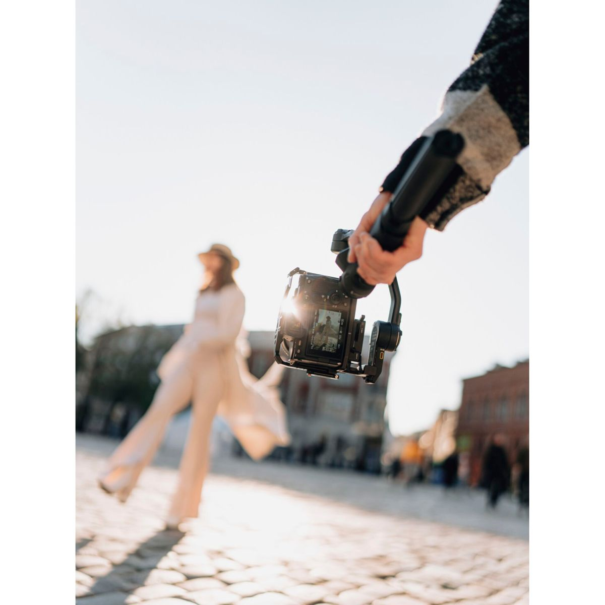 Eine Person hält eine Kamera auf einem Gimbal und erfasst eine verschwommene Figur in einer Straßenszene.
