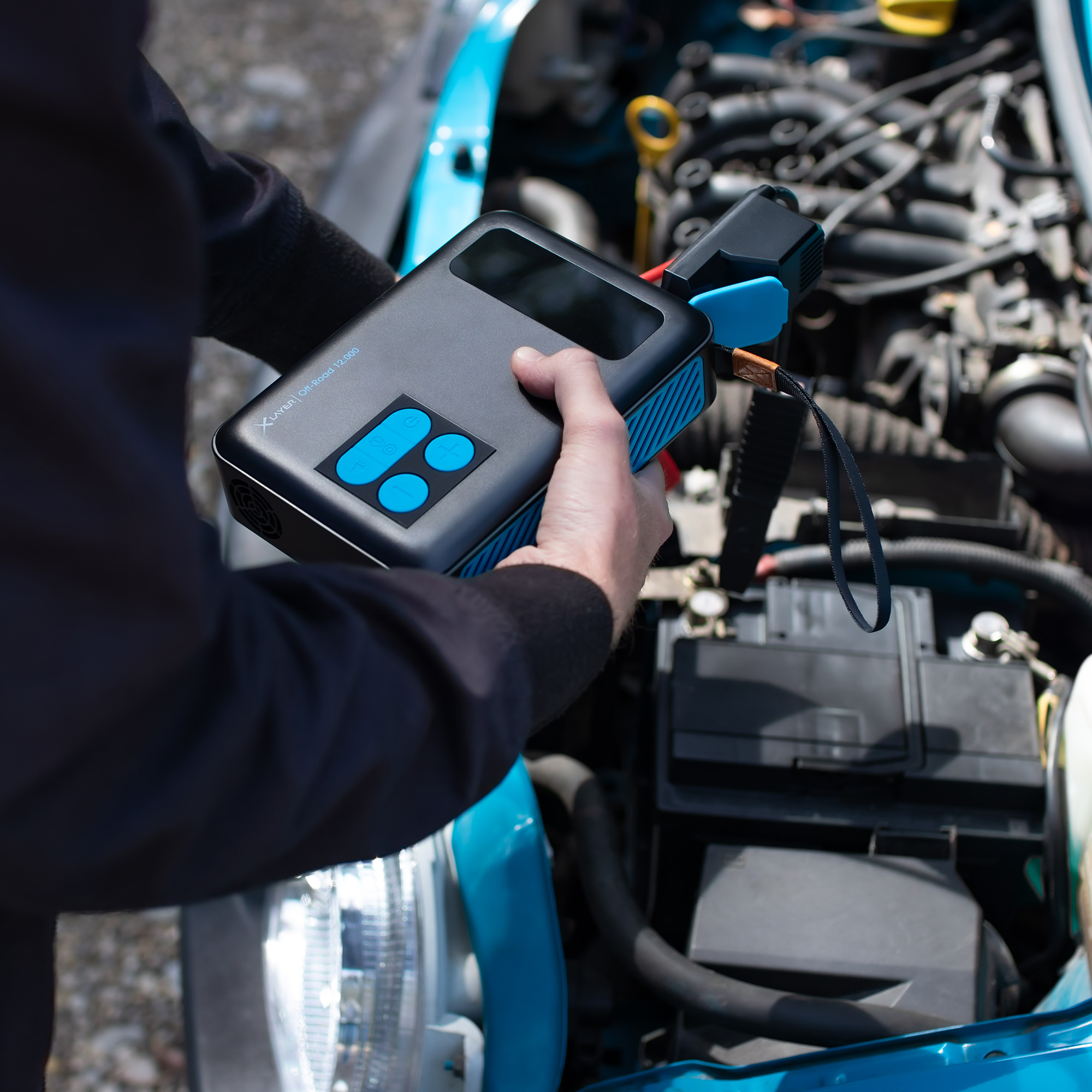 Eine Person hält einen schwarz-blauen Starthilfe für Autos in der Nähe eines offenen Motors.