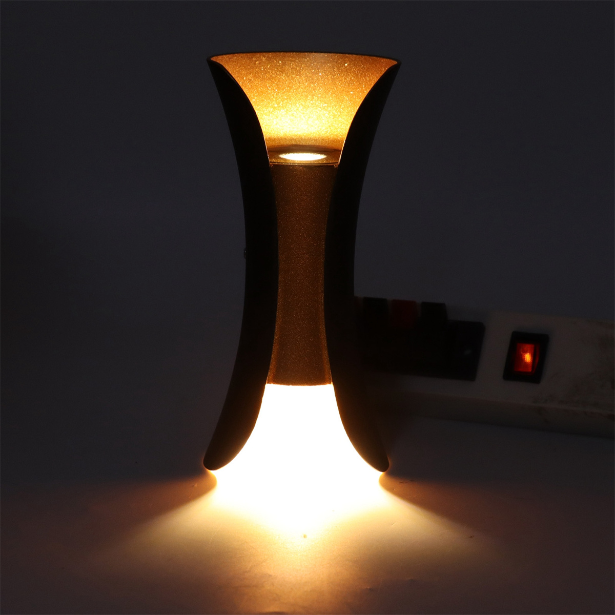 Wandleuchte mit goldenem Schein von oben und unten, auf dunklem Hintergrund.