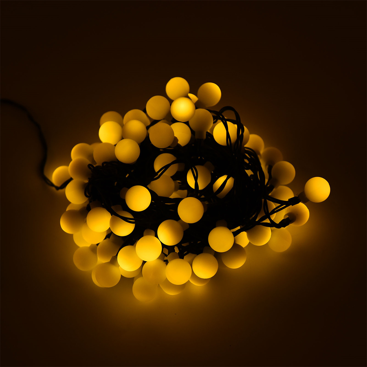 Eine Ansammlung gelber kugelförmiger Lichter auf einem schwarzen Kabel vor dunklem Hintergrund.