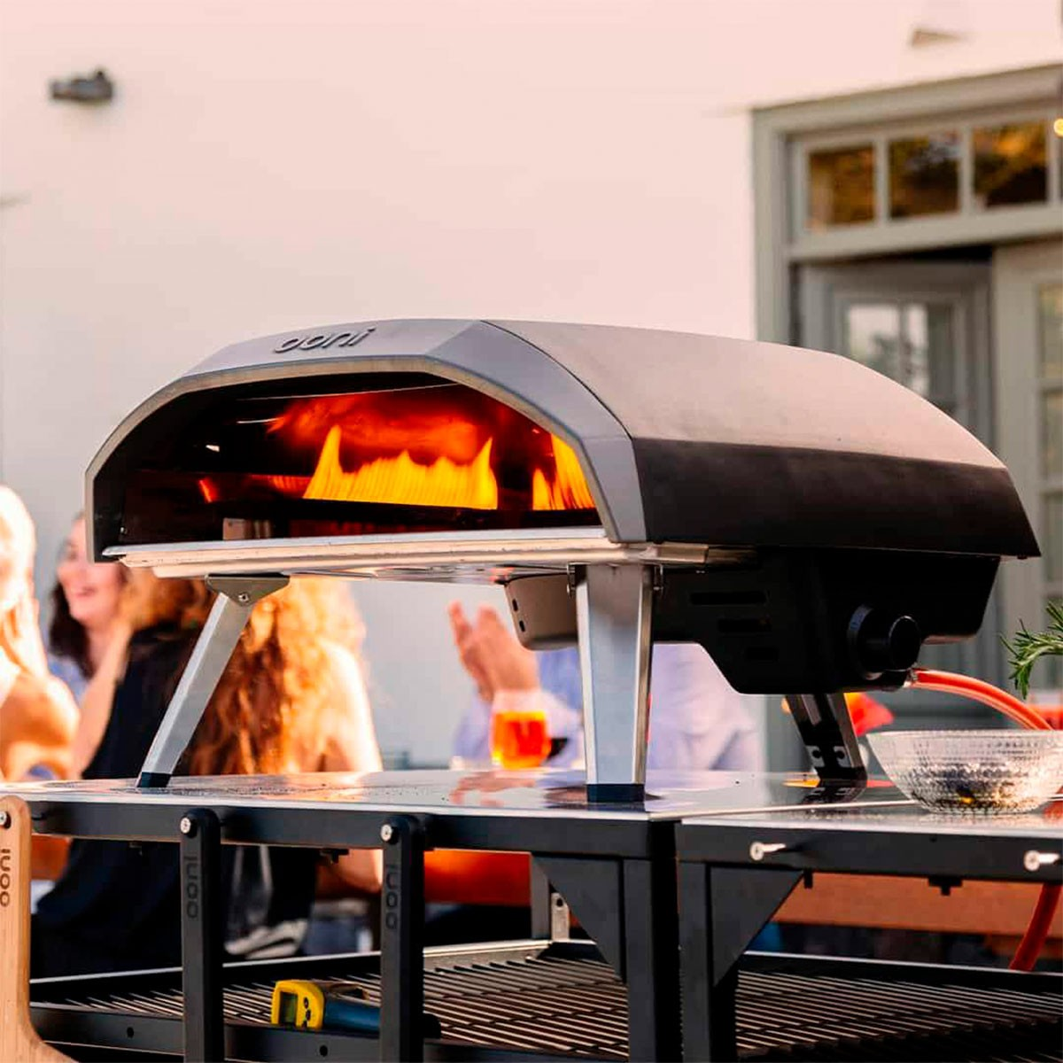 Un forno per pizza con fiamme all'interno. Persone sfocate sullo sfondo. Forno su un tavolo.