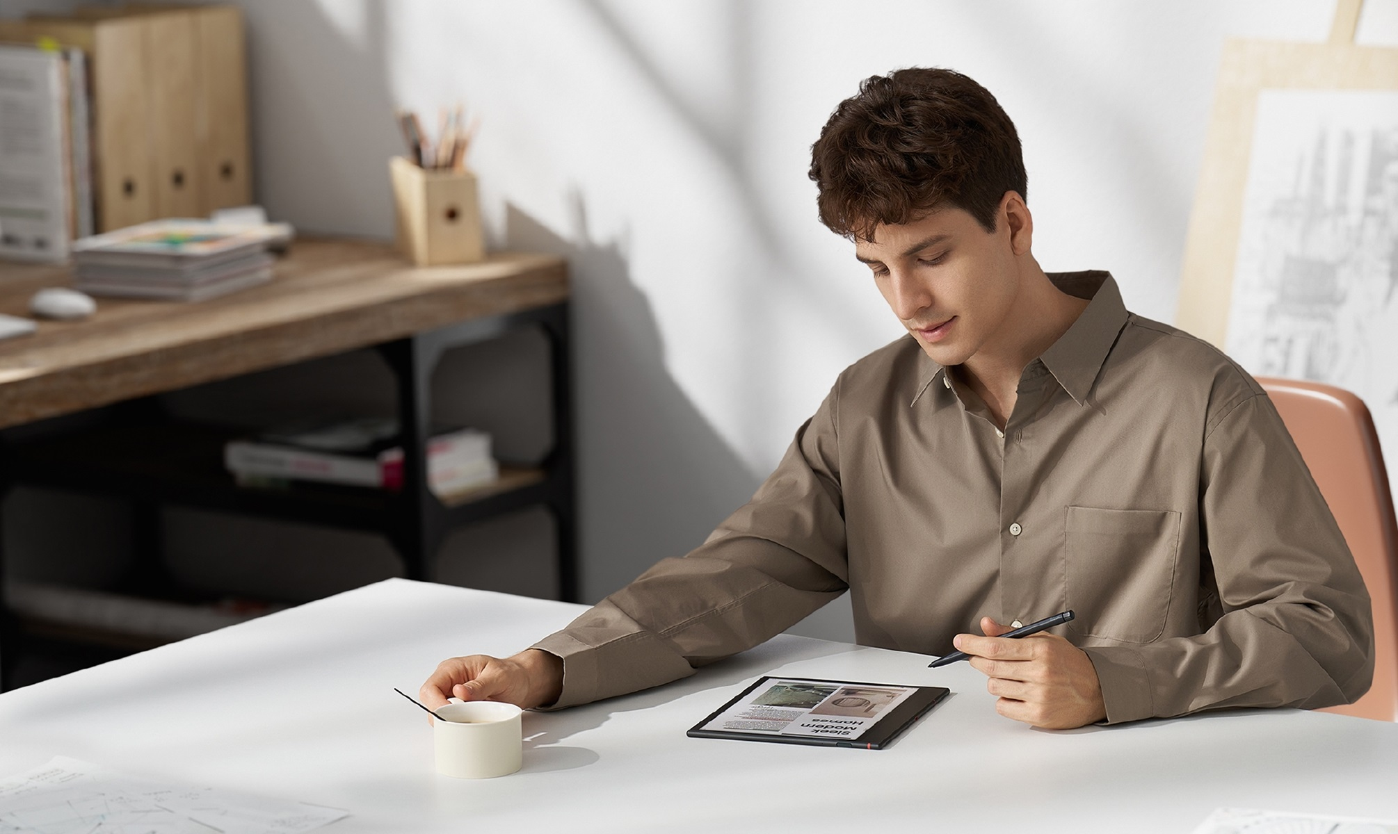 Mężczyzna siedzi przy biurku, używając tabletu z rysikiem. Na biurku są inne przedmioty.