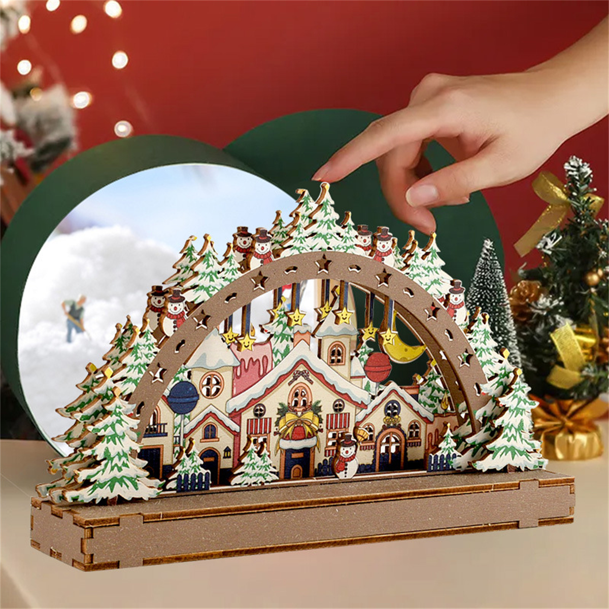 Weihnachtsdorf aus Holz mit Schneemännern, Bögen und Lichtern, mit einer Hand, die in die Szene greift.
