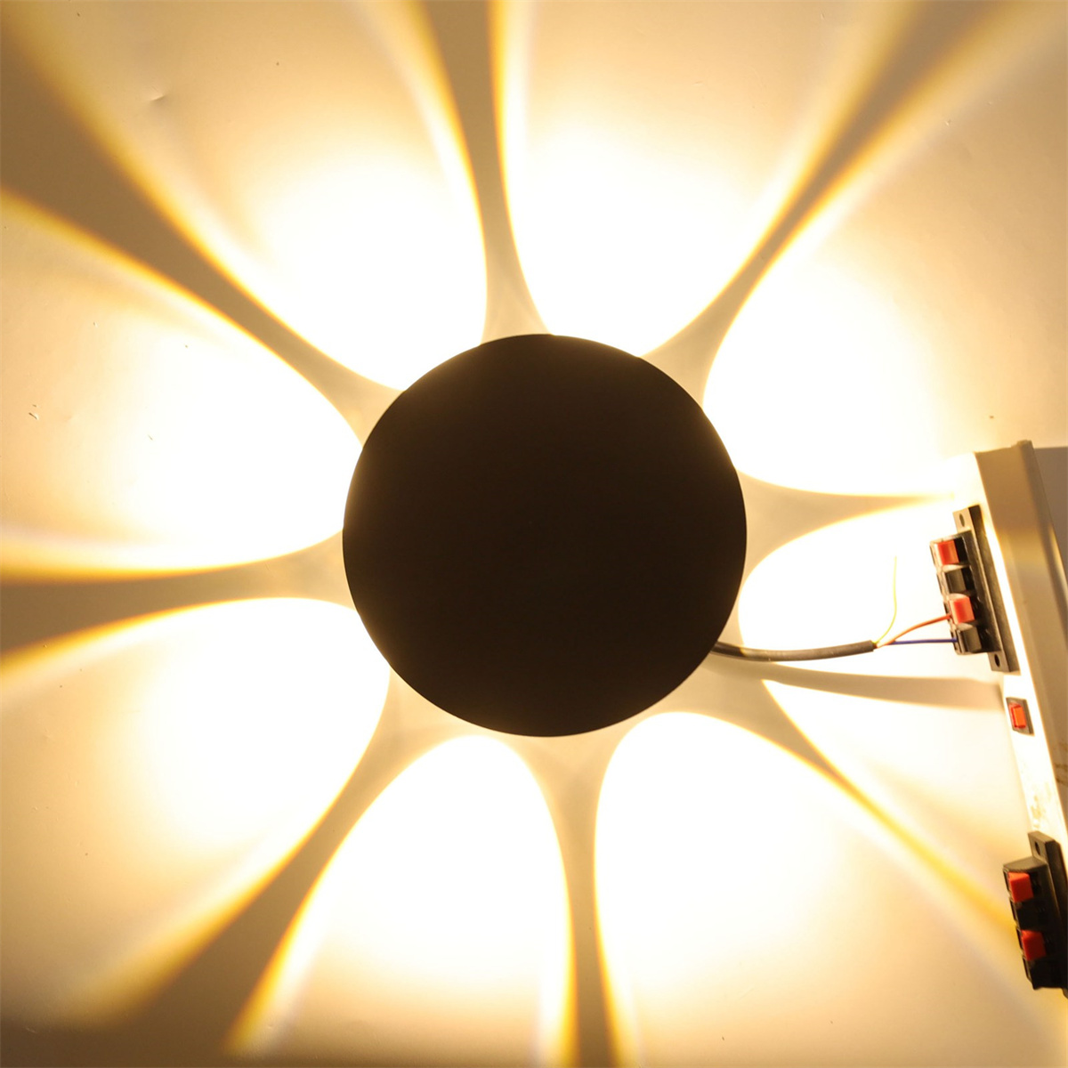 Eine schwarze Wandleuchte mit kreisförmigem Licht und mehreren Lichtstrahlen.