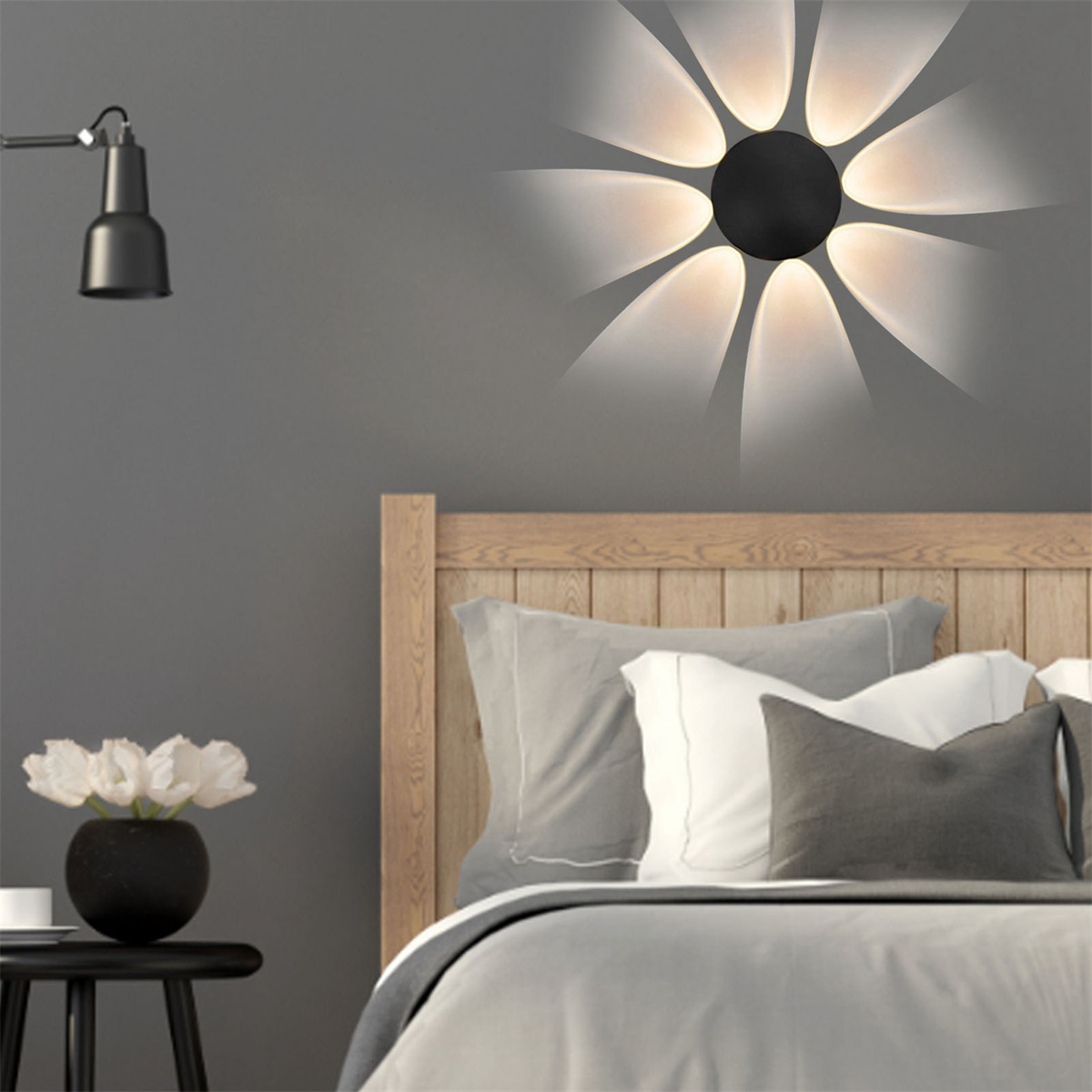 Eine blütenförmige Leuchte an einer grauen Wand. Die Lichter scheinen auf ein Bett.