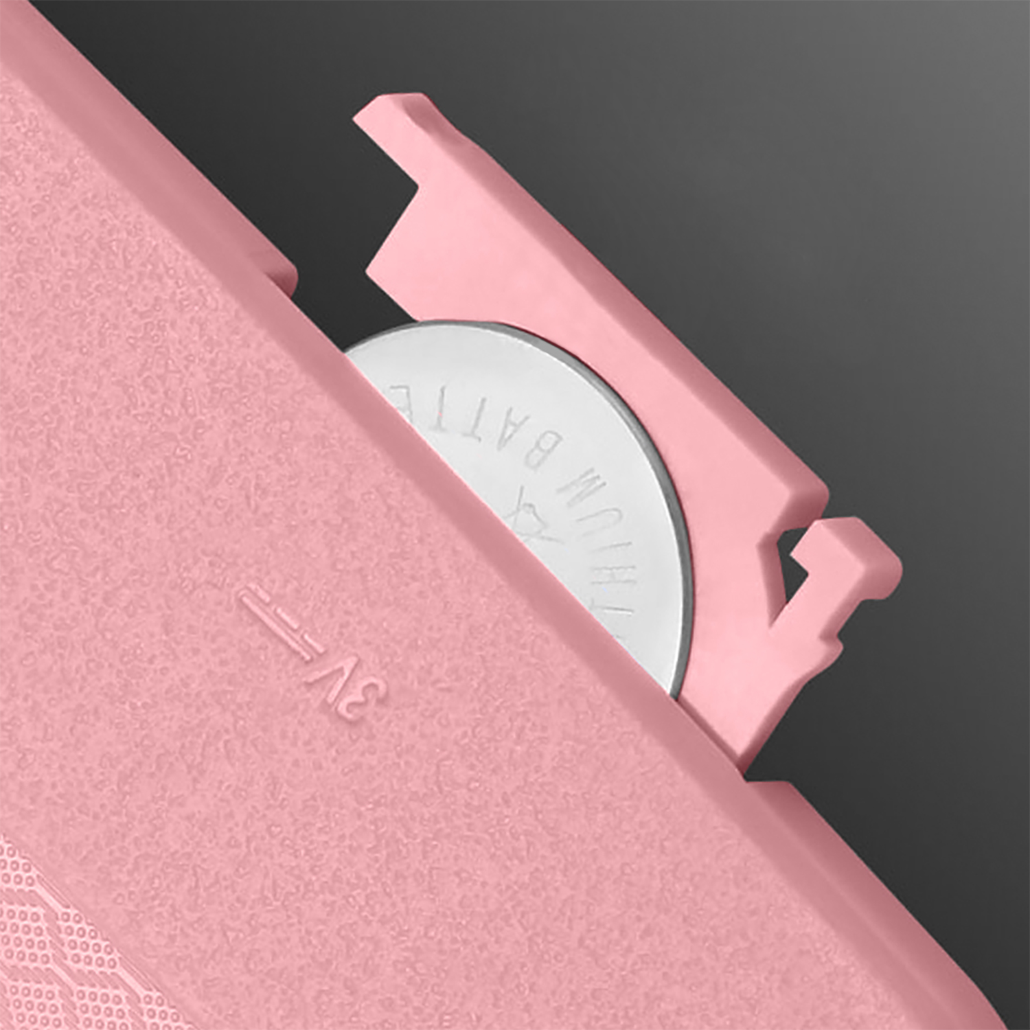 Un vano batteria rosa con una batteria argentata all'interno, accanto a una superficie rosa.