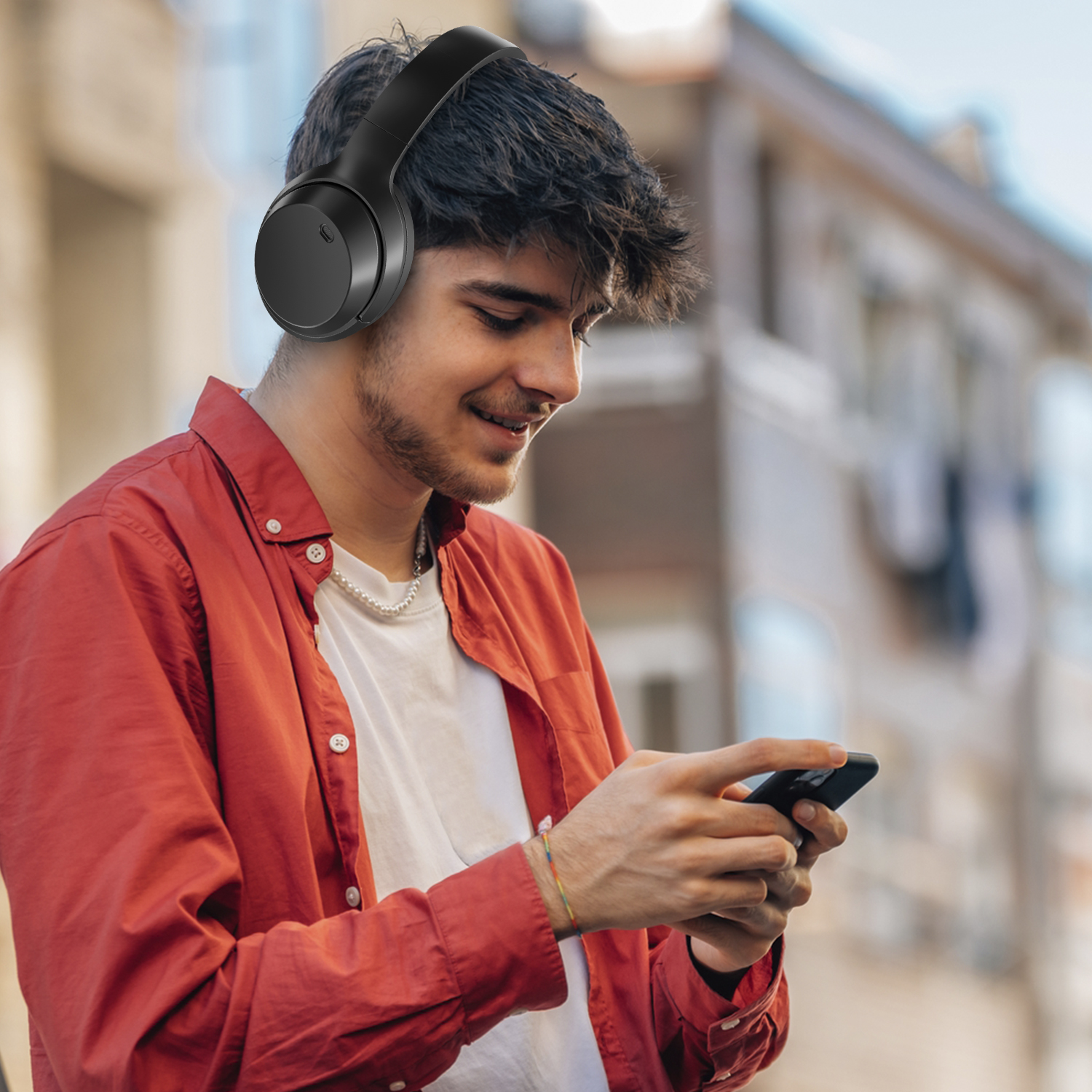 Uomo con cuffie e camicia rossa, che guarda il telefono. Sfondo sfocato.