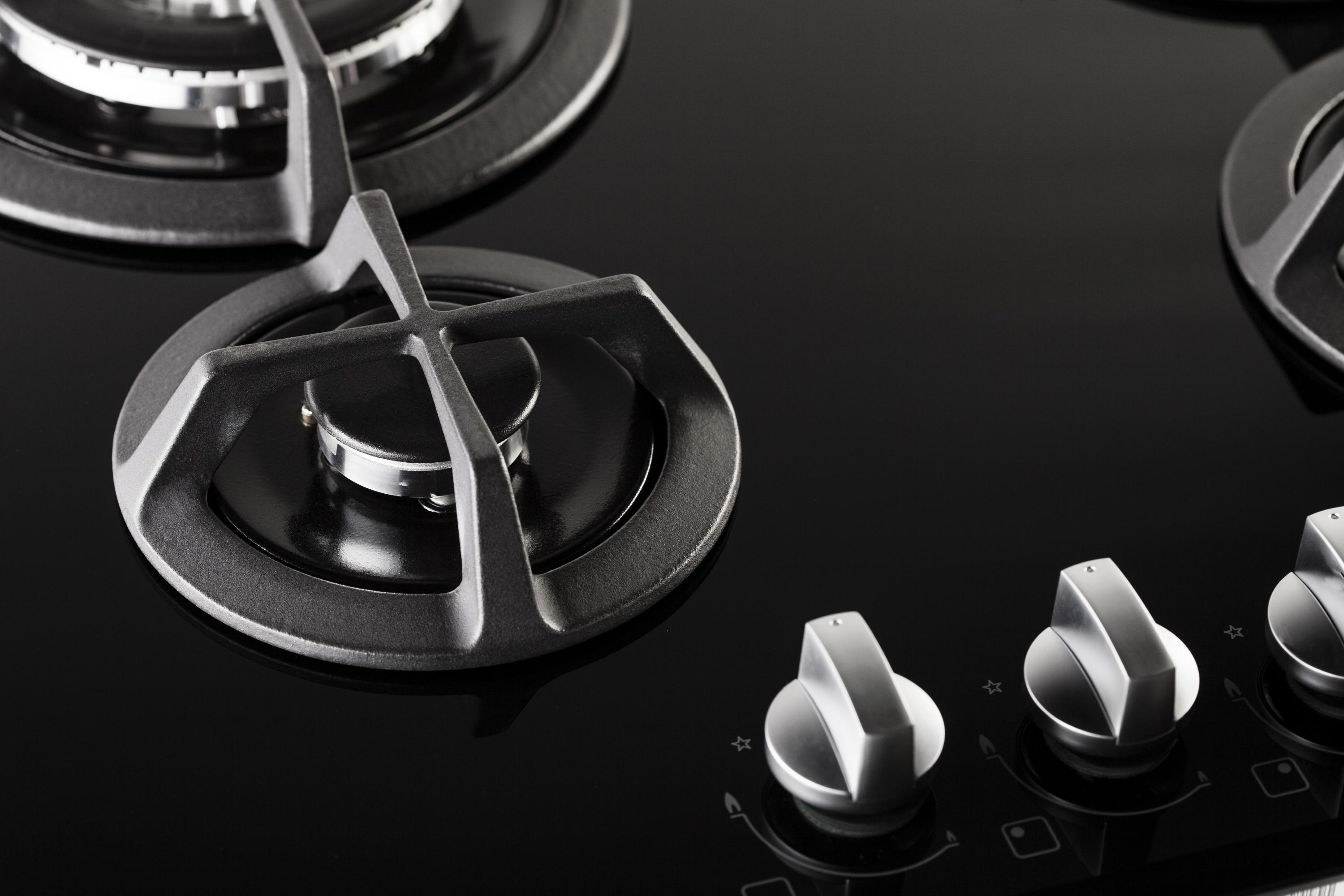 Primo piano di un piano cottura a gas in vetro nero con quattro bruciatori e manopole. Il design è moderno.