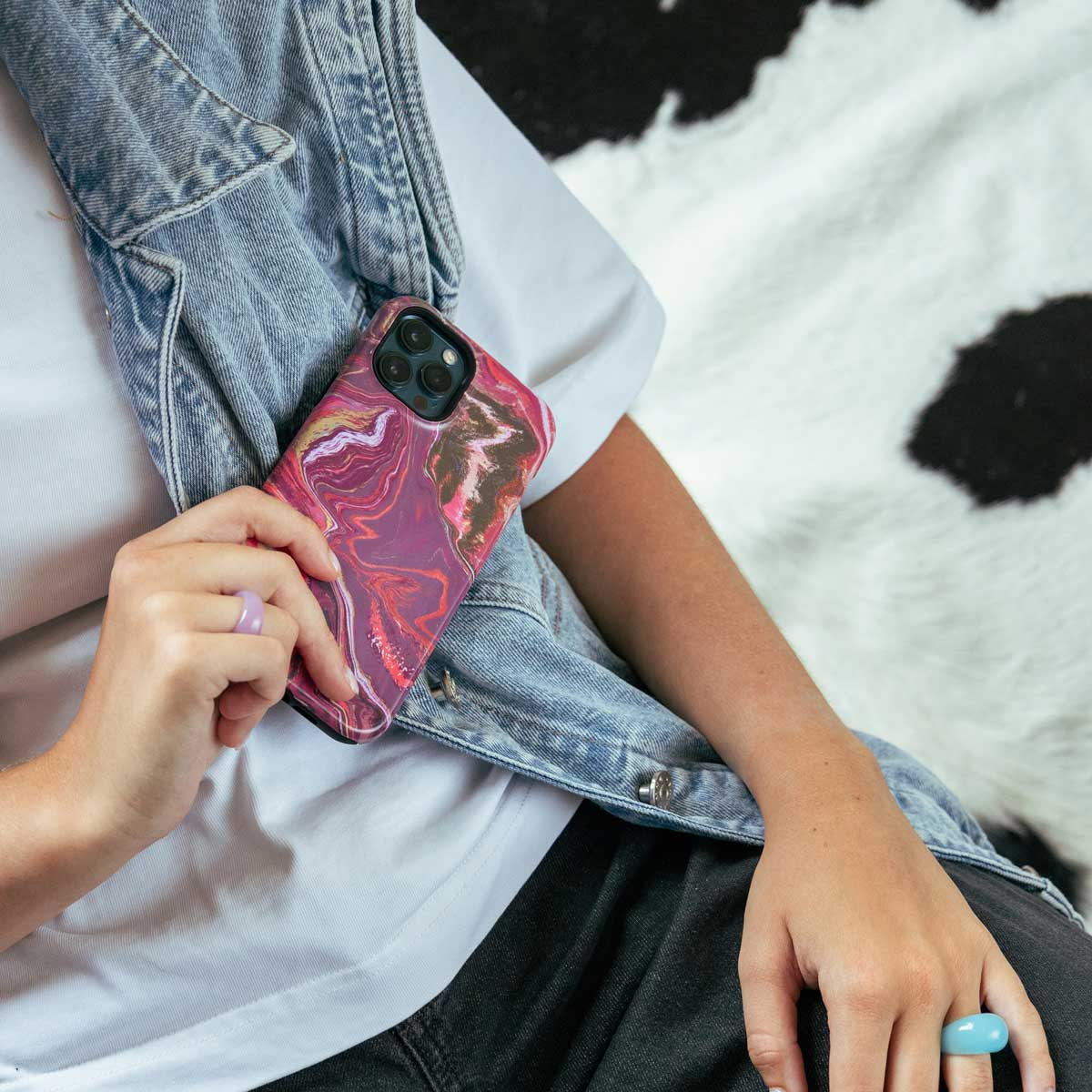 Een vrouw met een spijkerjasje en ringen die een telefoon vasthoudt met een roze marmeren hoesje.