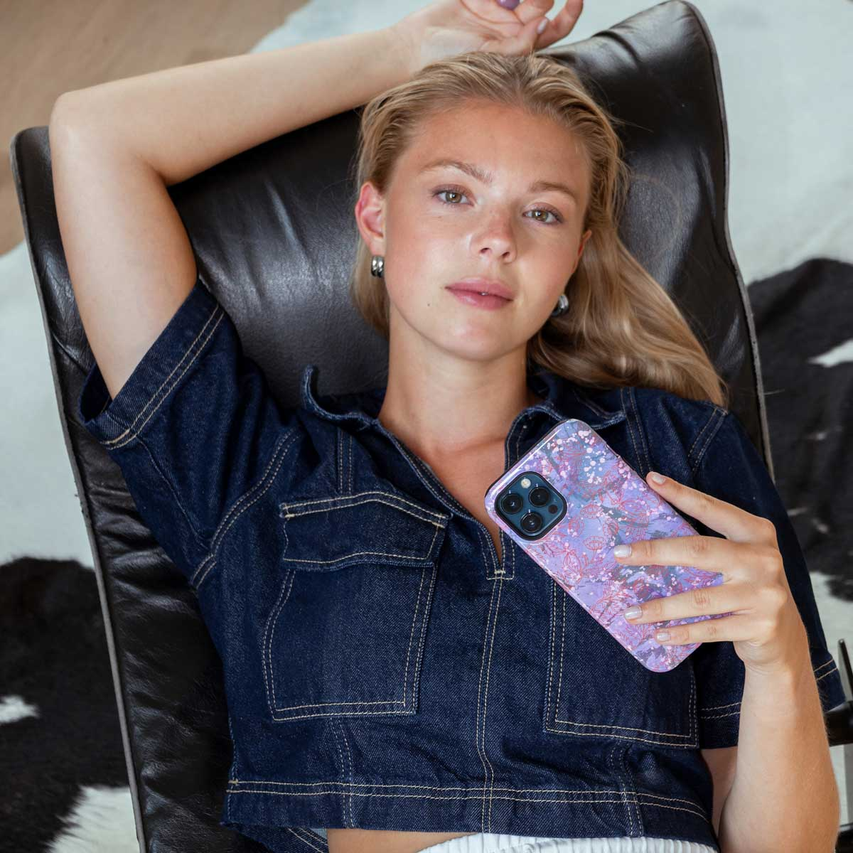 Een vrouw in een spijkeroverhemd ligt op een stoel, met een telefoon met een bloemenhoes.