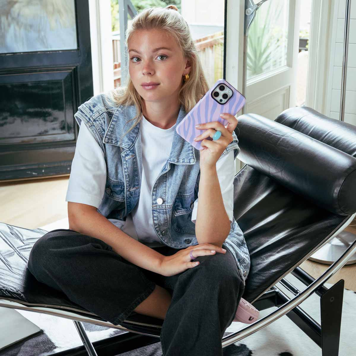 Blonde vrouw die zit en een telefoon vasthoudt met een paarse, patroonhoes.
