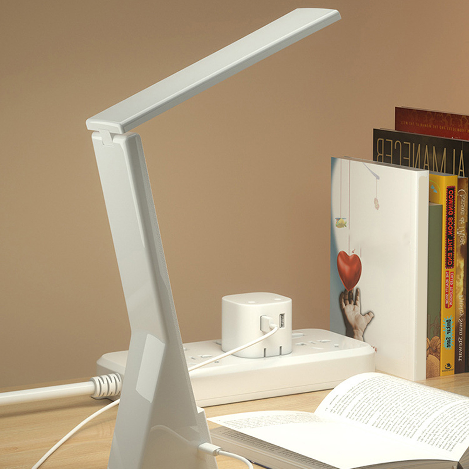 Weiße Schreibtischlampe mit Büchern und Steckdosenleiste auf einem Schreibtisch.