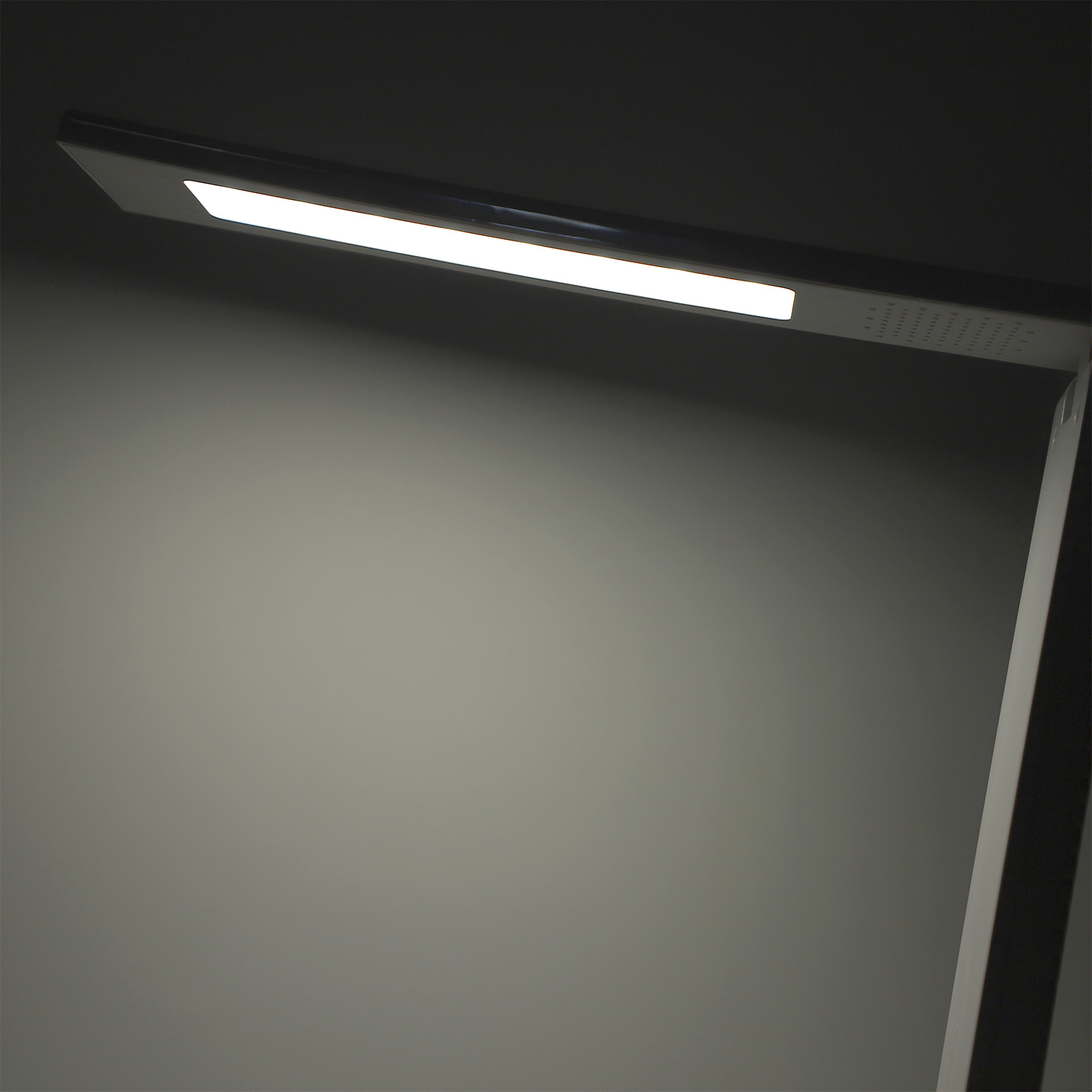 Eine moderne Schreibtischlampe mit hellem LED-Lichtstreifen, der ein sanftes Leuchten vor einem dunkelgrauen Hintergrund erzeugt.