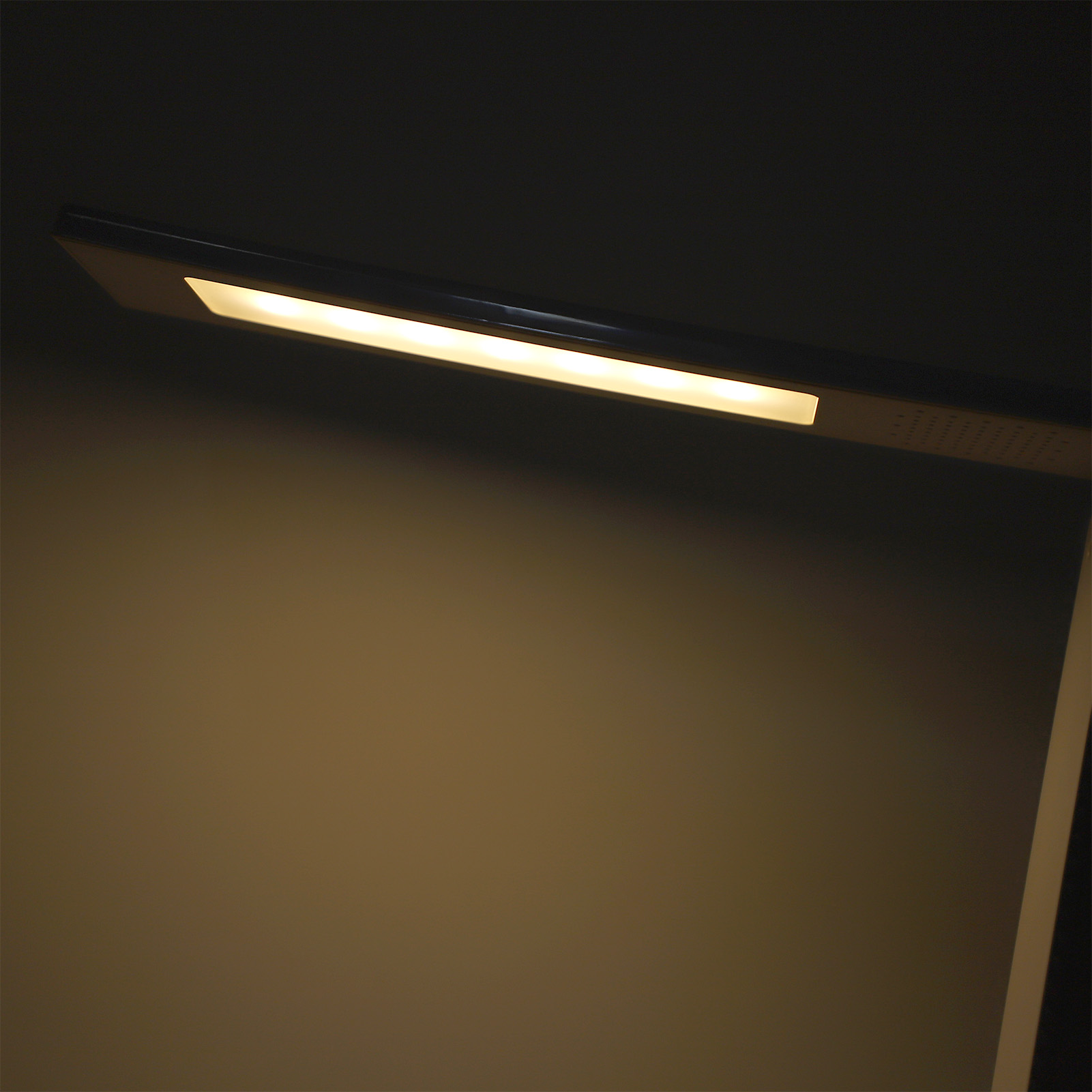 Eine moderne Schreibtischlampe mit hellem Licht vor dunklem Hintergrund.
