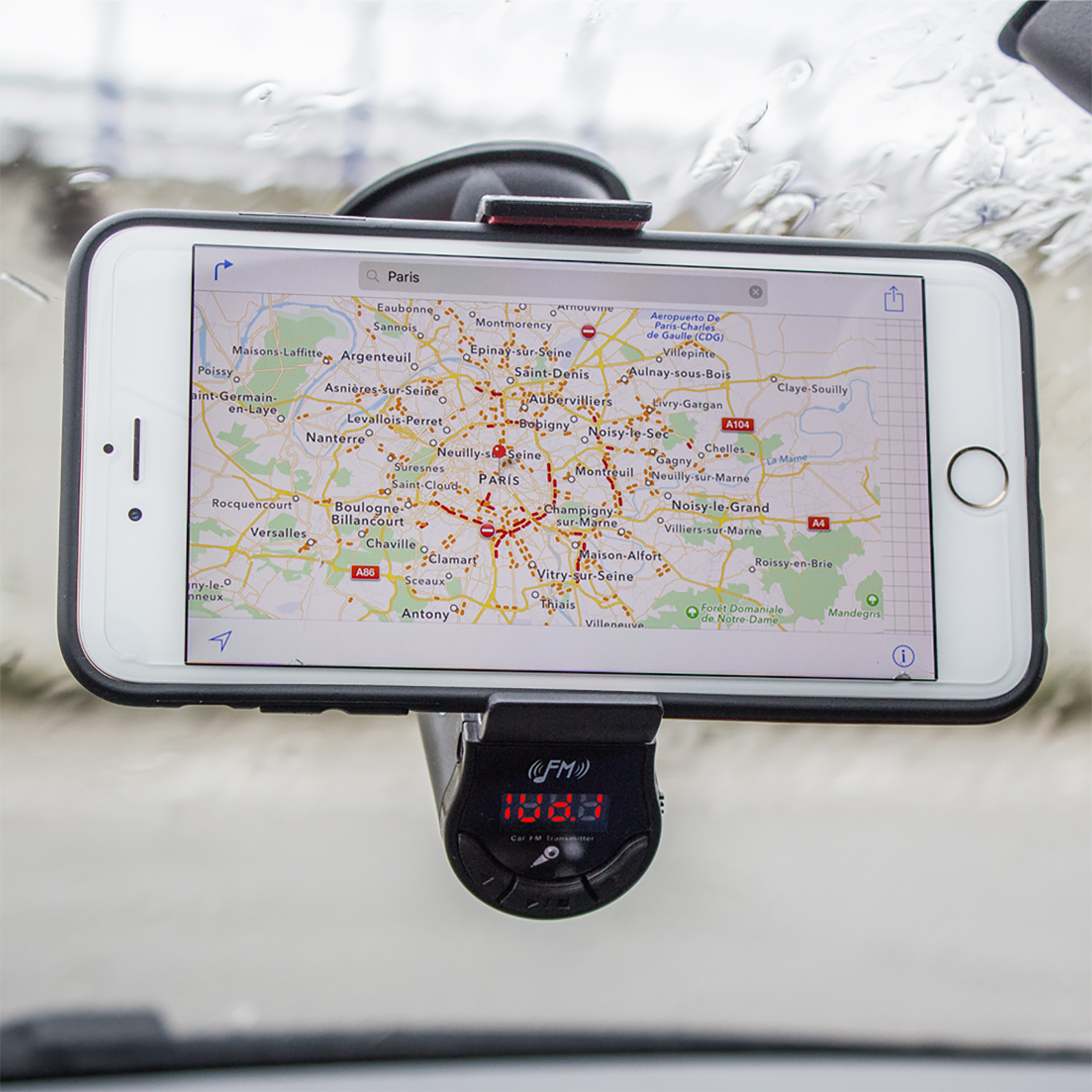 Un teléfono en un soporte para automóvil muestra un mapa de París. Debajo hay un transmisor FM.