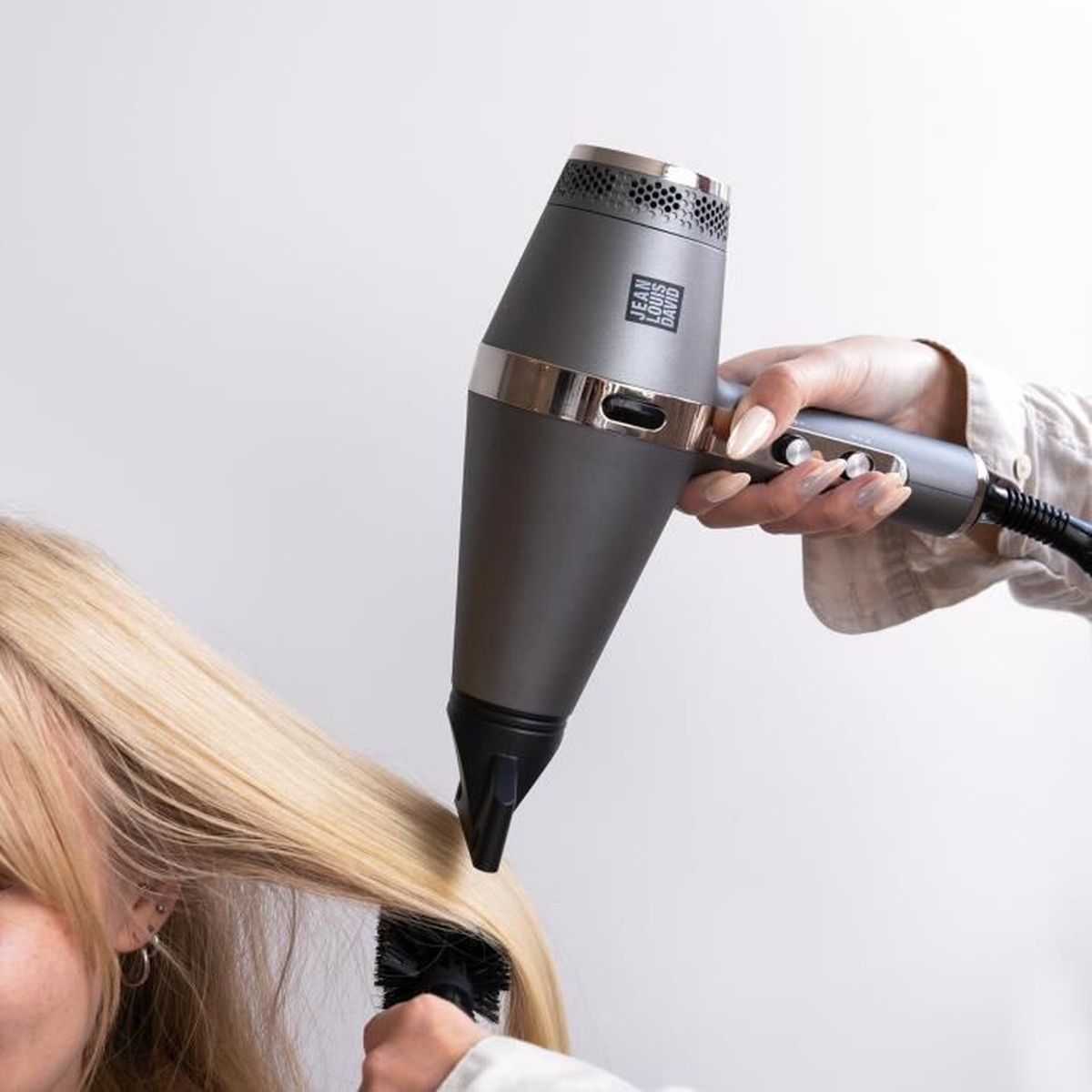 Mujer usando un secador de pelo, secando cabello rubio con un cepillo.