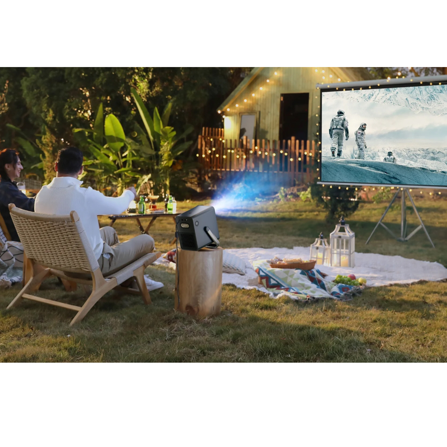 Leute schauen einen Film, der in einem Garten auf eine Leinwand projiziert wird. Mit Projektor.