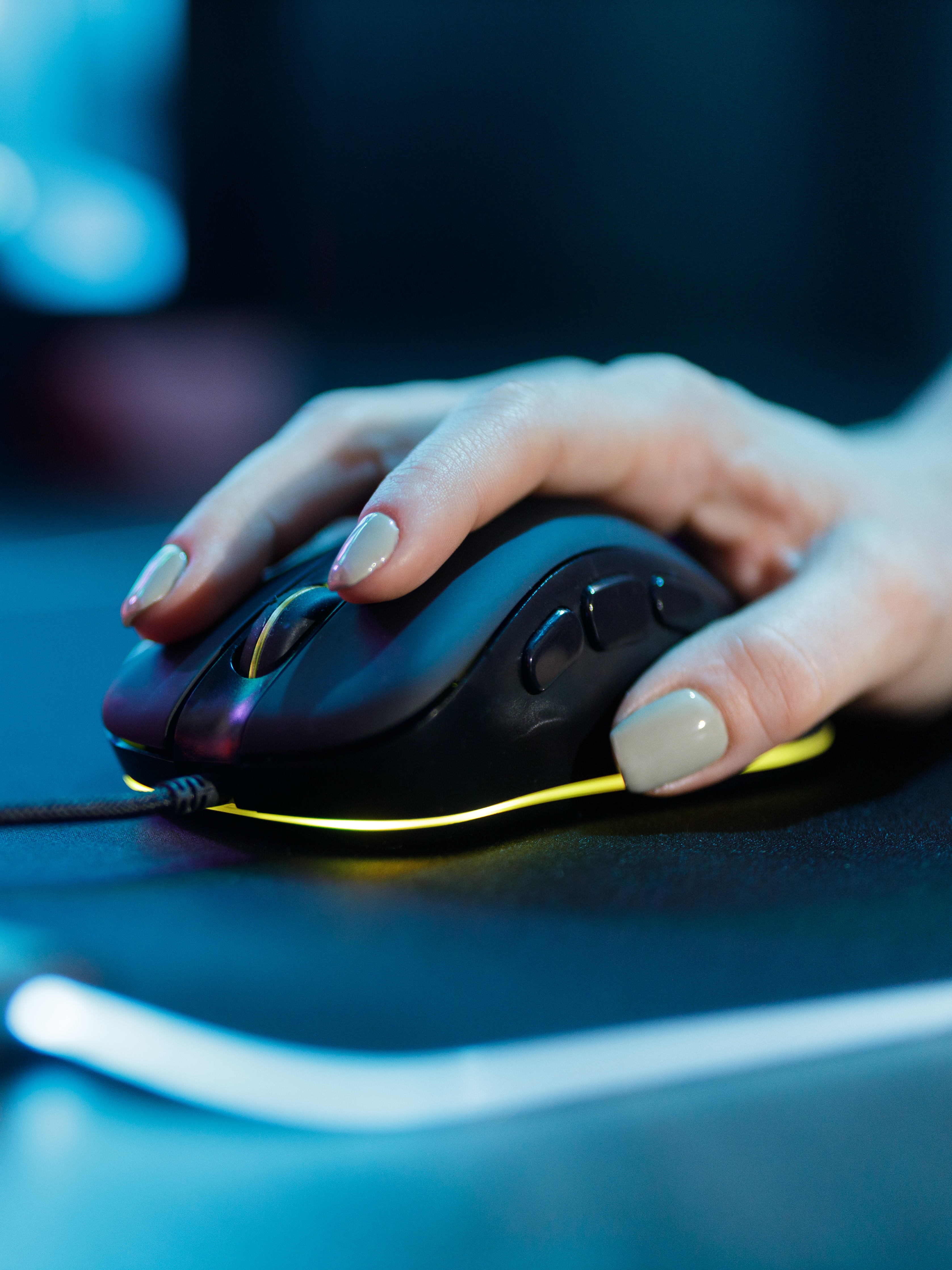 Dłoń trzymająca czarną mysz na ciemnej powierzchni z niebieskim oświetleniem.