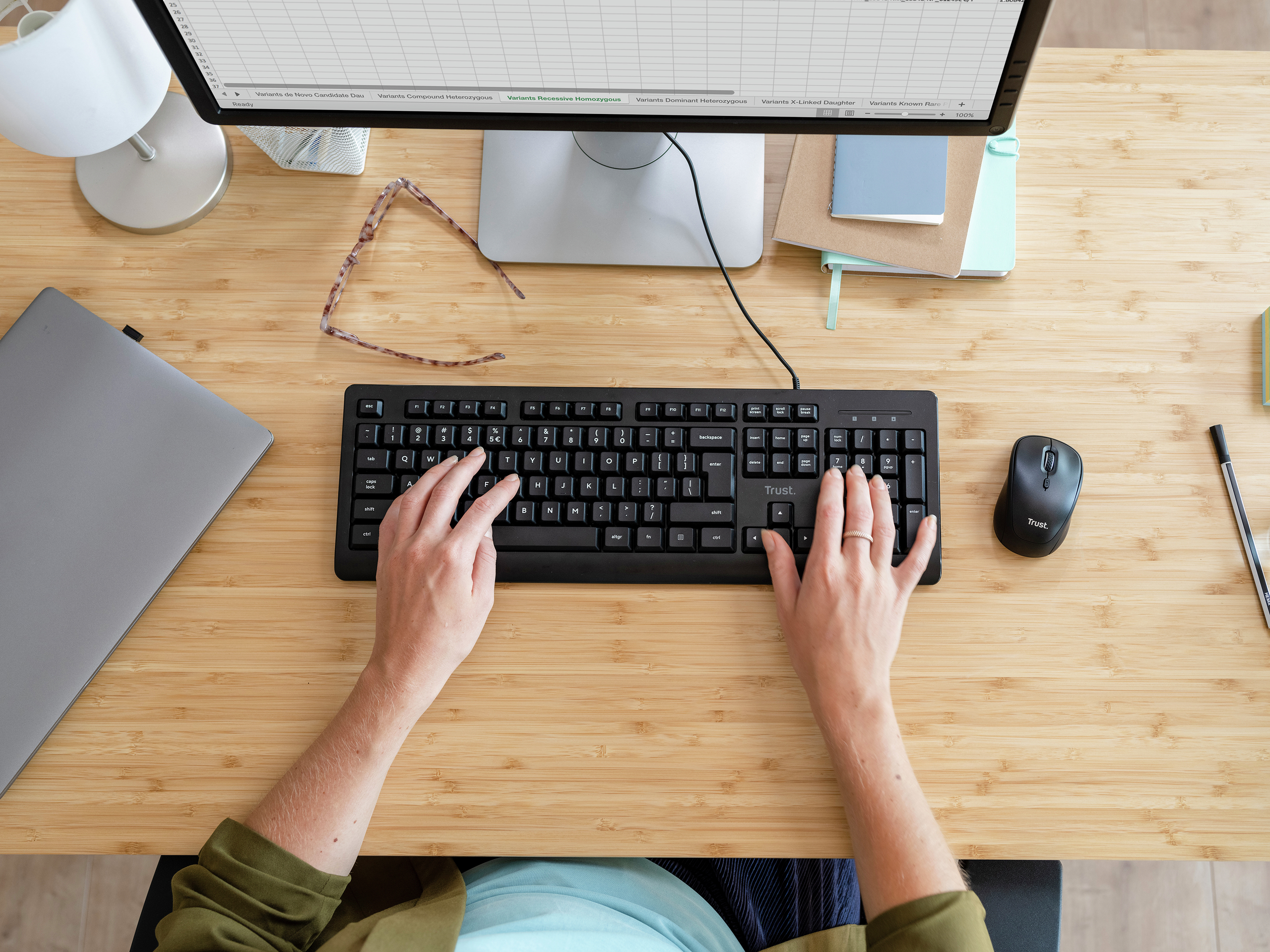 Ręce osoby na czarnej klawiaturze i myszy na drewnianym biurku z monitorem.
