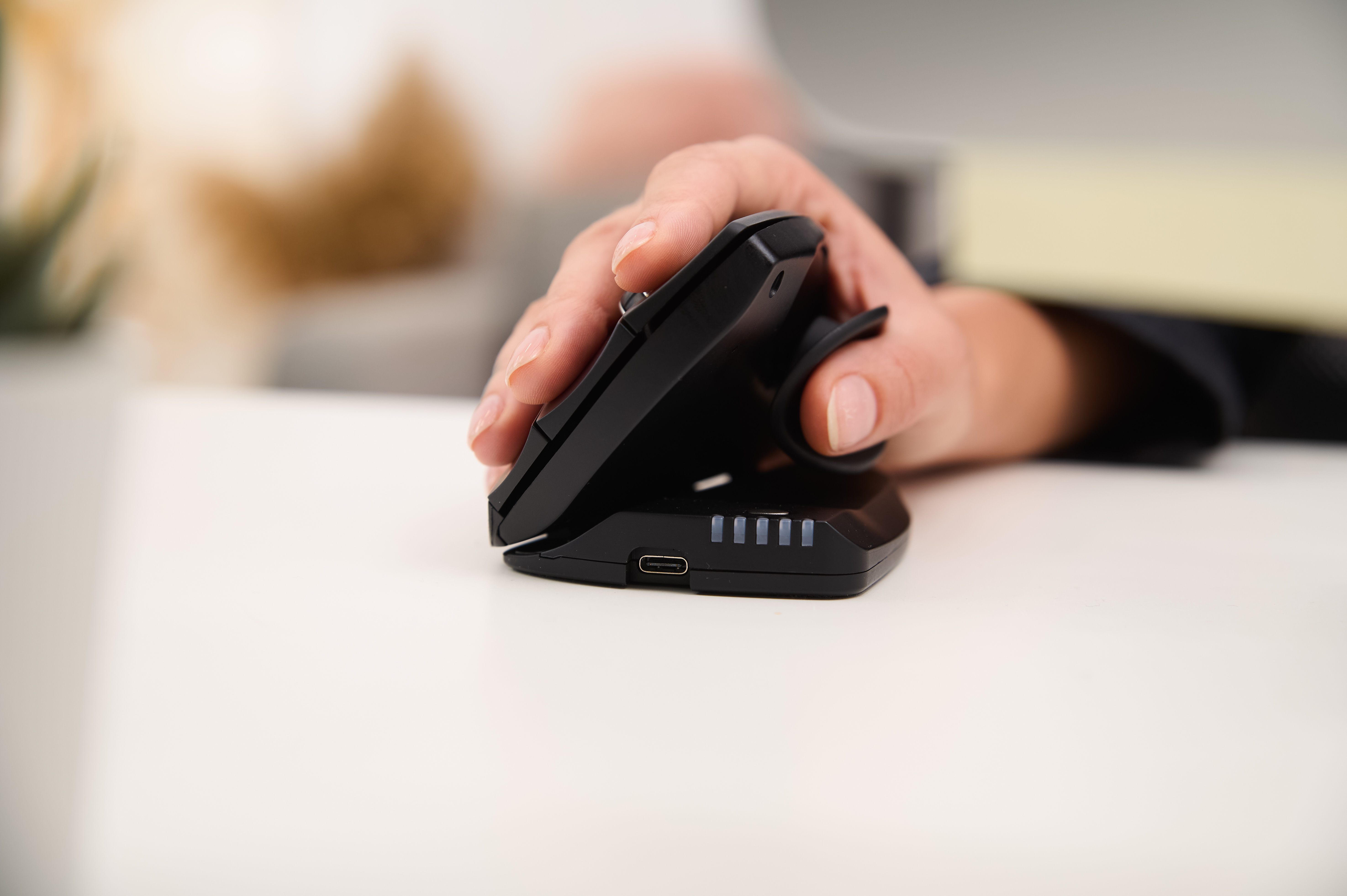 Een hand die een zwarte ergonomische muis boven een oplaadbasis houdt, met zichtbare knoppen.