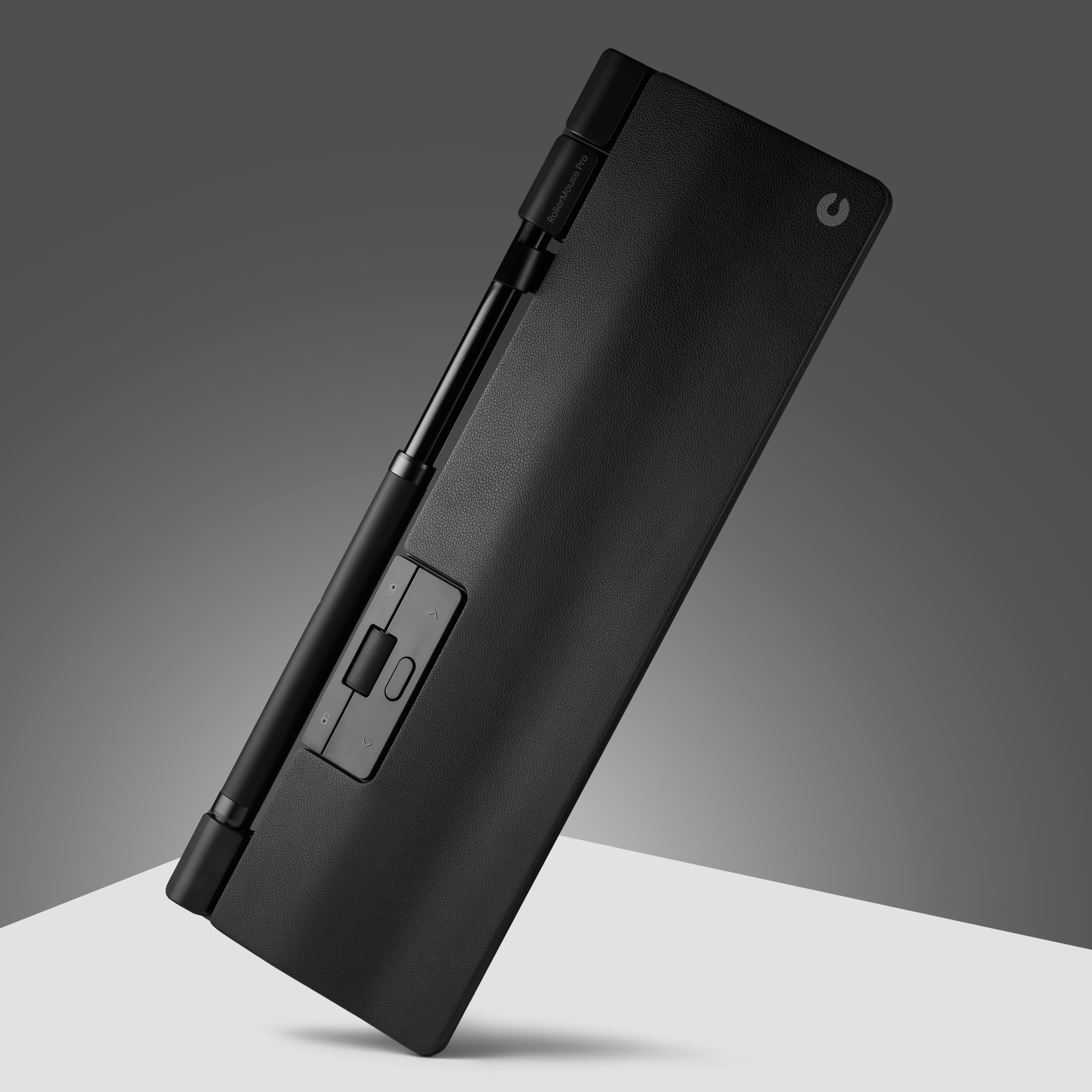 Czarna mysz rolkowa, pochylona, na białej powierzchni i szarym tle.