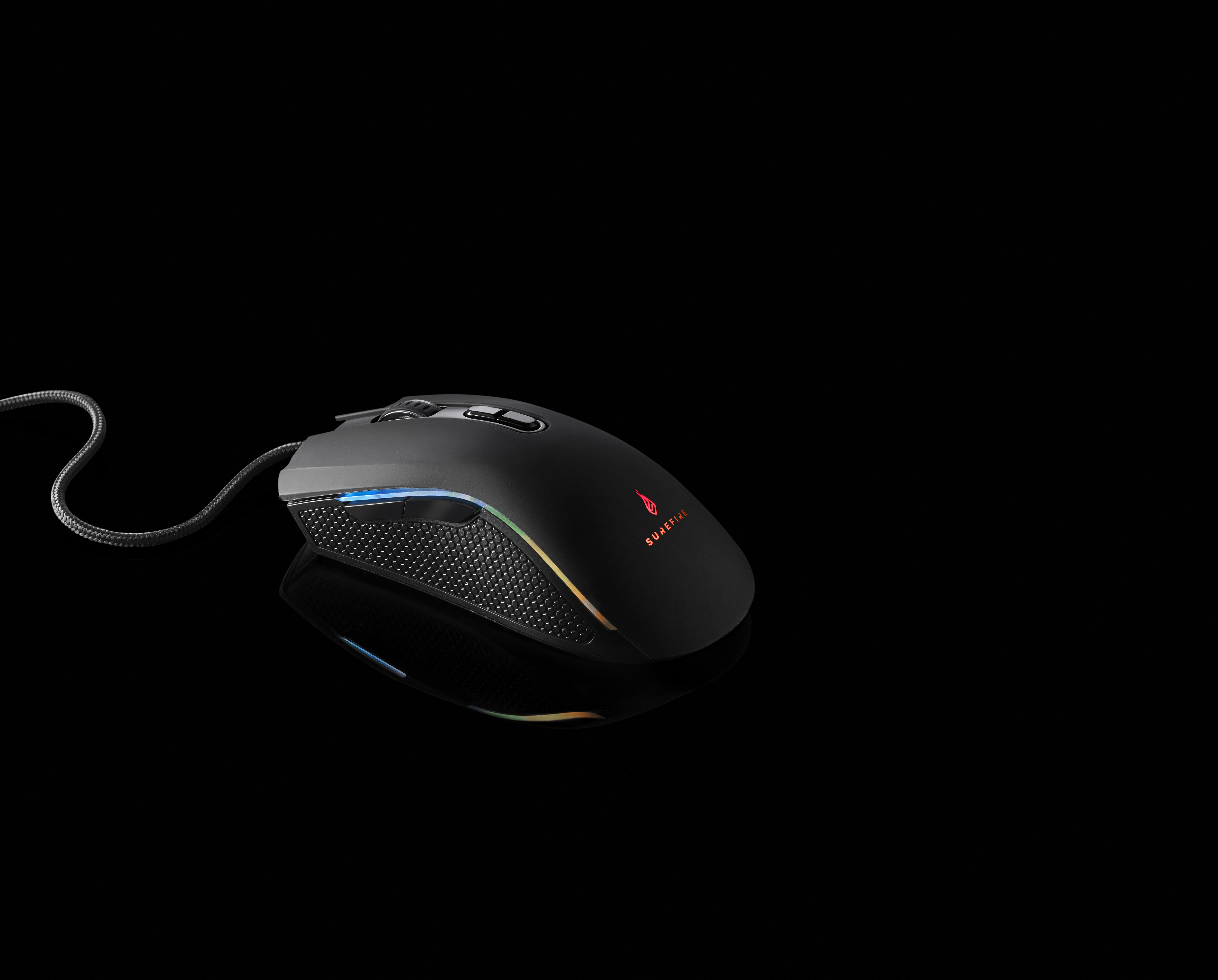 Un mouse da gaming nero su una superficie nera, con un cavo. Ha un lato a rete e un logo che si illumina.