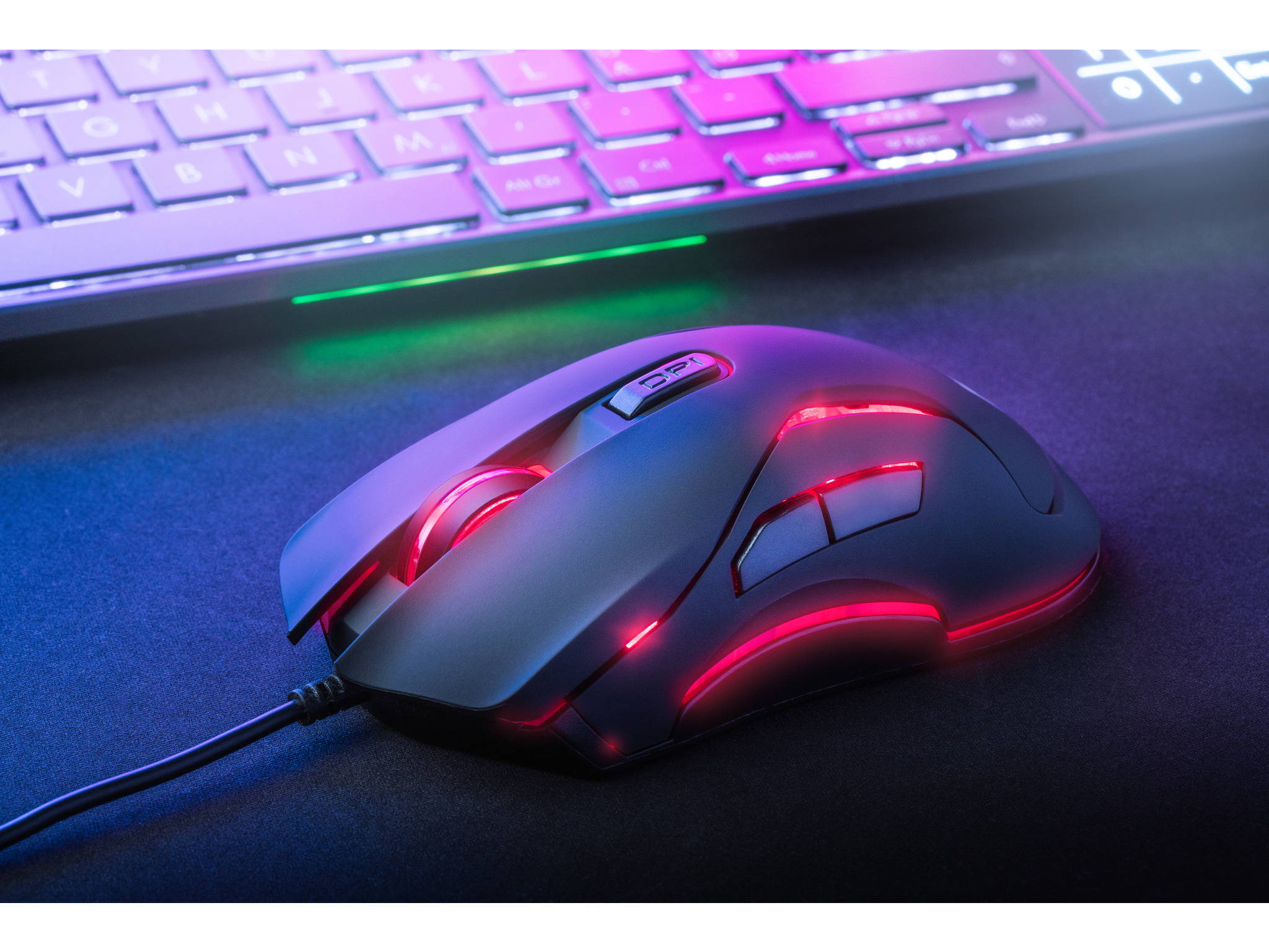 Gaming mouse on a desk, illuminated with red and blue lights, near a keyboard.