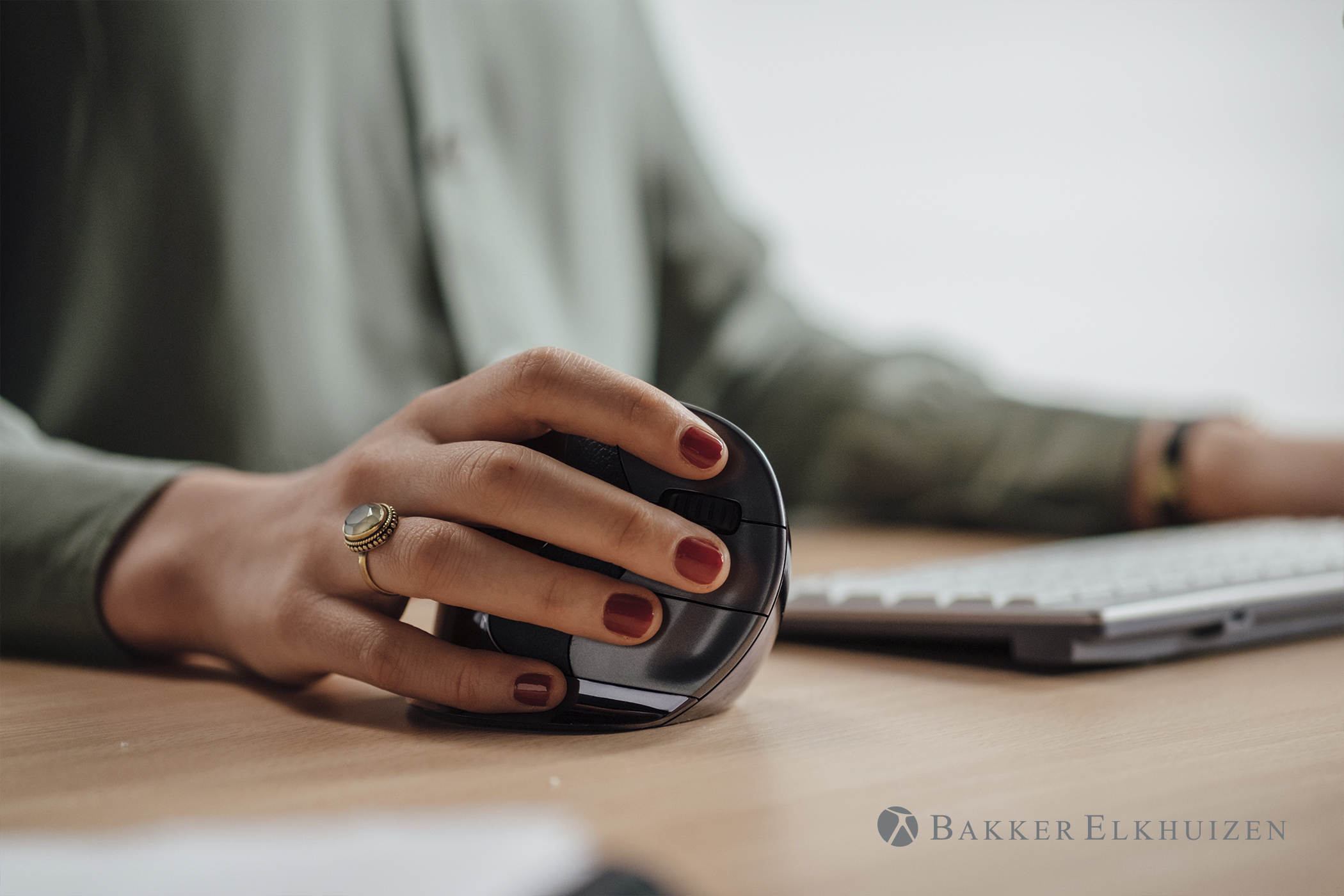 Hand holding an ergonomic mouse. The mouse is black and brown. The person is wearing a ring.