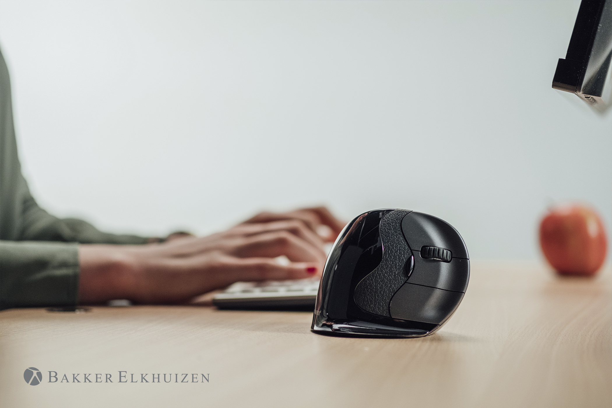 Person typing on keyboard with black vertical mouse beside, on a wooden desk.