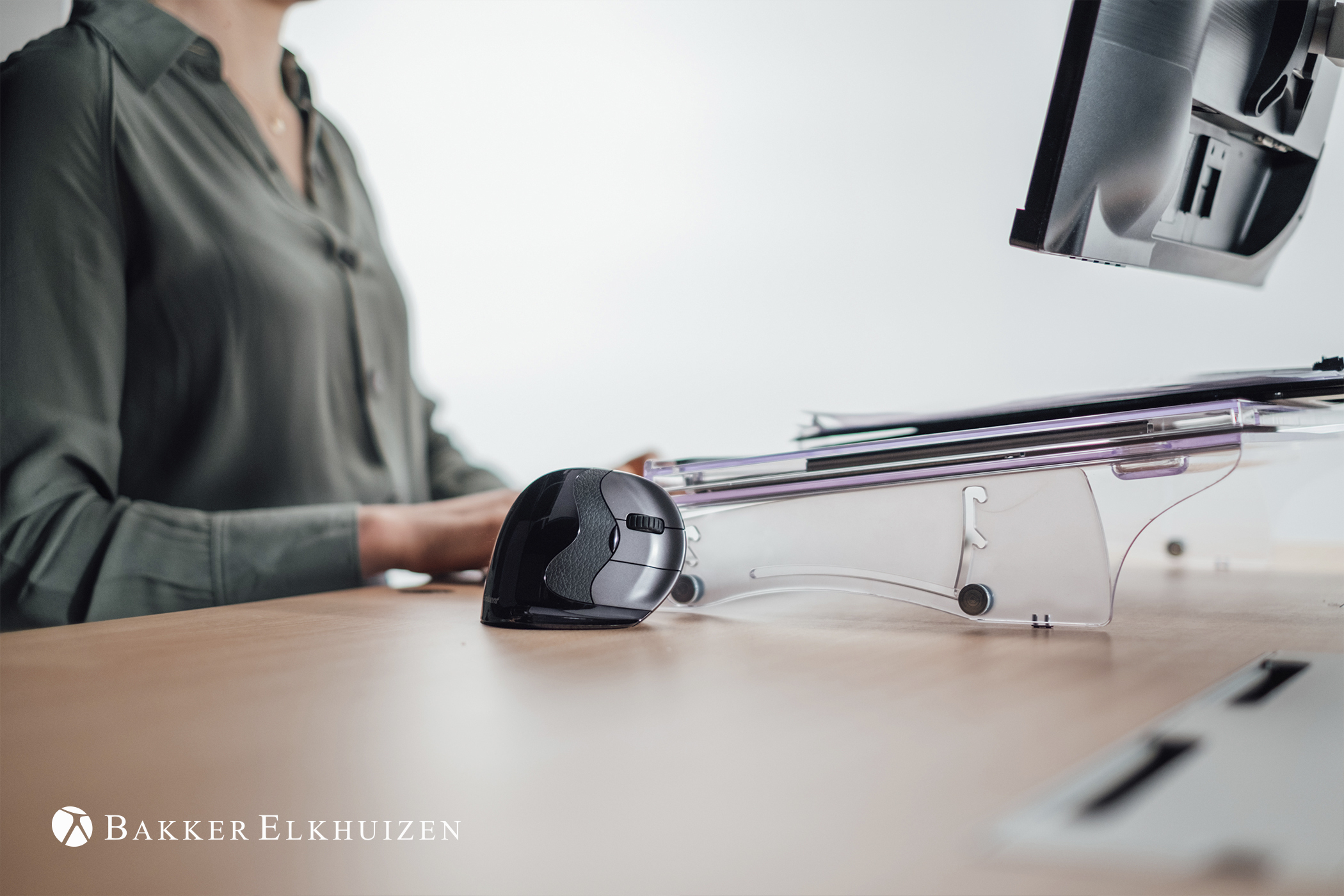 Woman's hands near a black mouse on a desk. Monitor and desk setup.