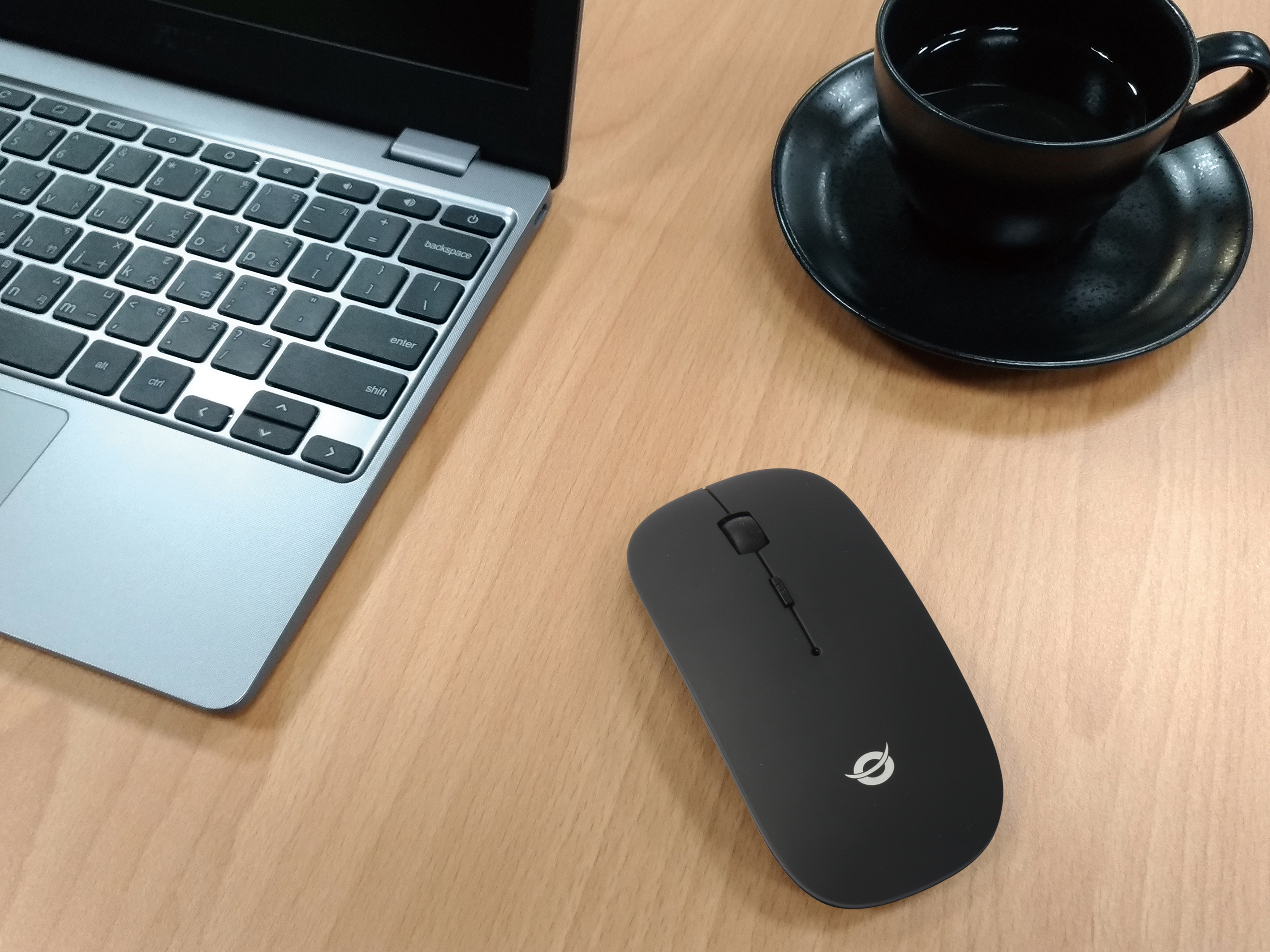 Zwarte muis op een houten bureau naast een laptop en een kopje koffie.