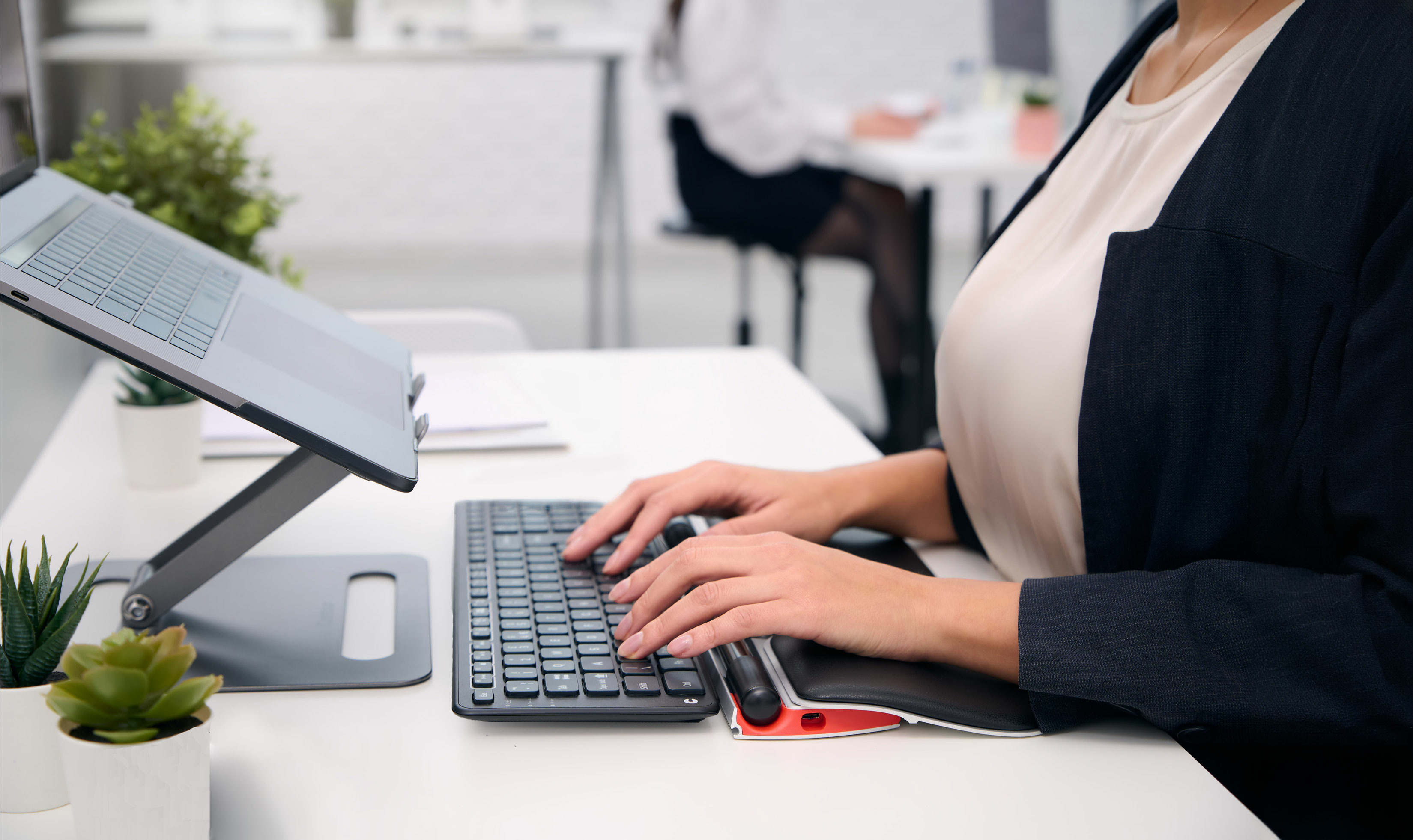 Woman working on a laptop and a keyboard on a white desk. A mouse is also present.