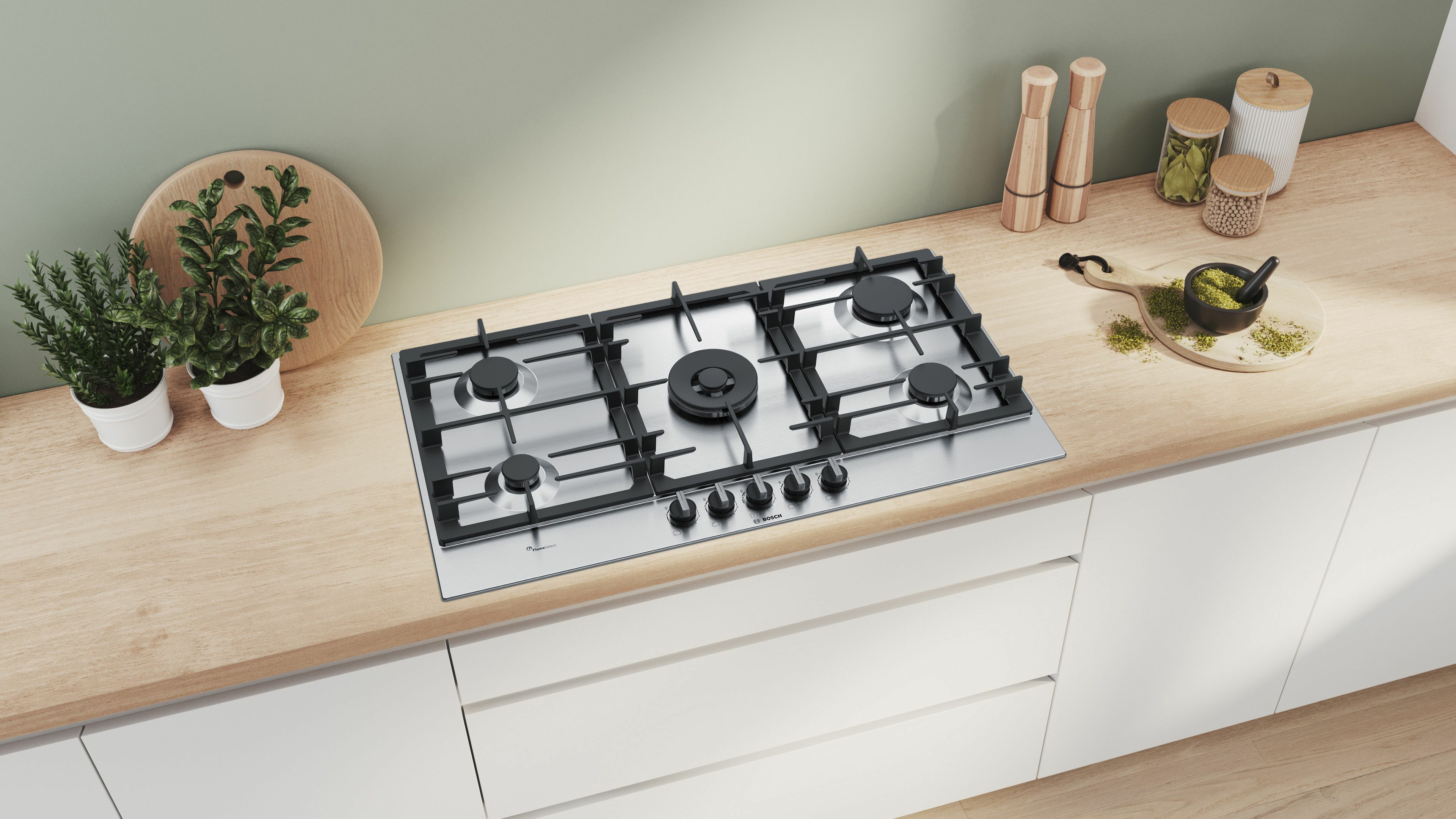 Piano cottura a gas in acciaio inox con bruciatori, su un piano di lavoro in legno con mobili bianchi.