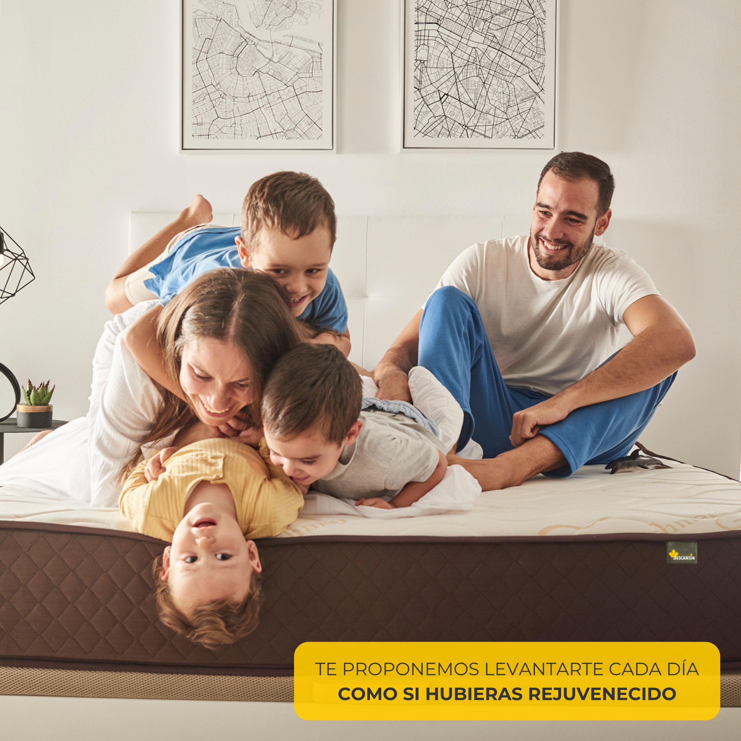 Familia en una cama. Padres sonriendo, niños jugando. Están acostados en un colchón marrón.