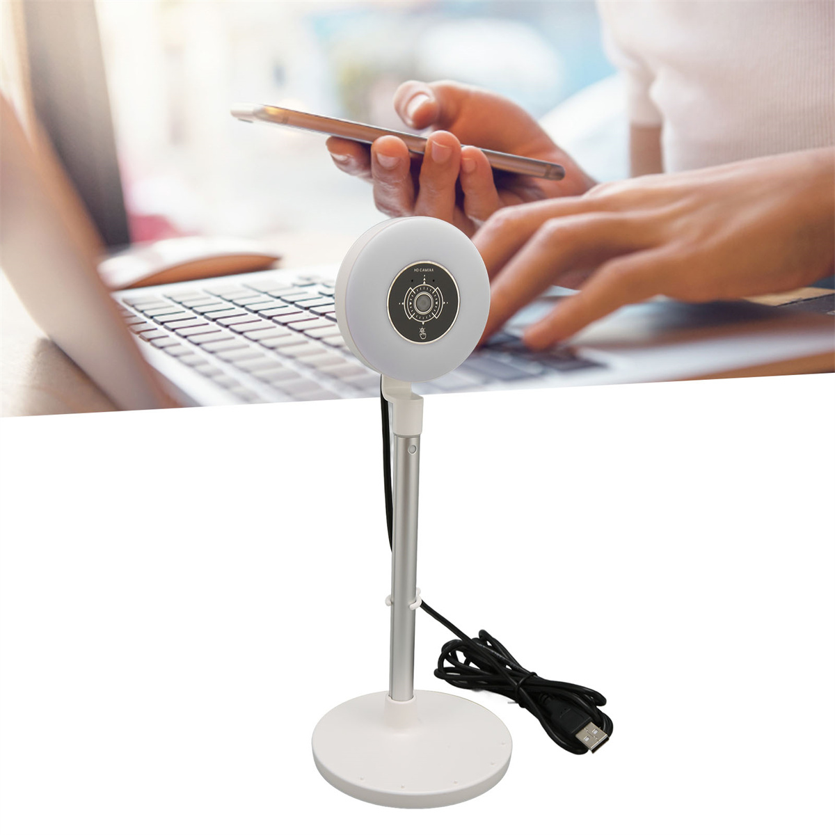 Eine weiße Schreibtischlampe mit Ständer und USB-Kabel. Eine Person benutzt im Hintergrund einen Laptop.