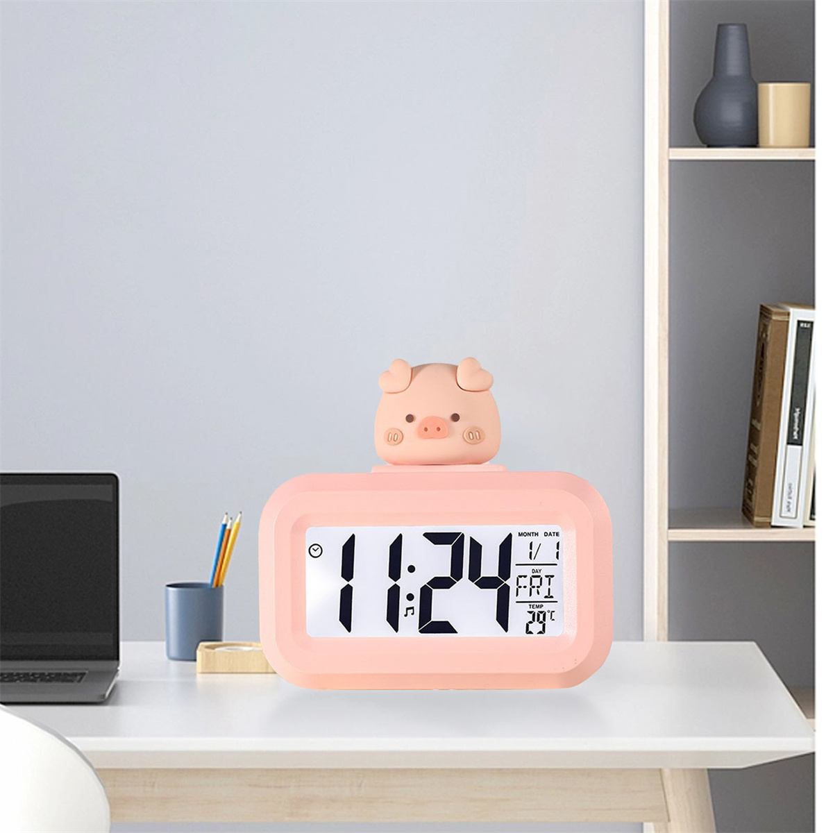 Rosa schweineförmiger digitaler Wecker, der Zeit und Datum anzeigt, auf einem weißen Schreibtisch.