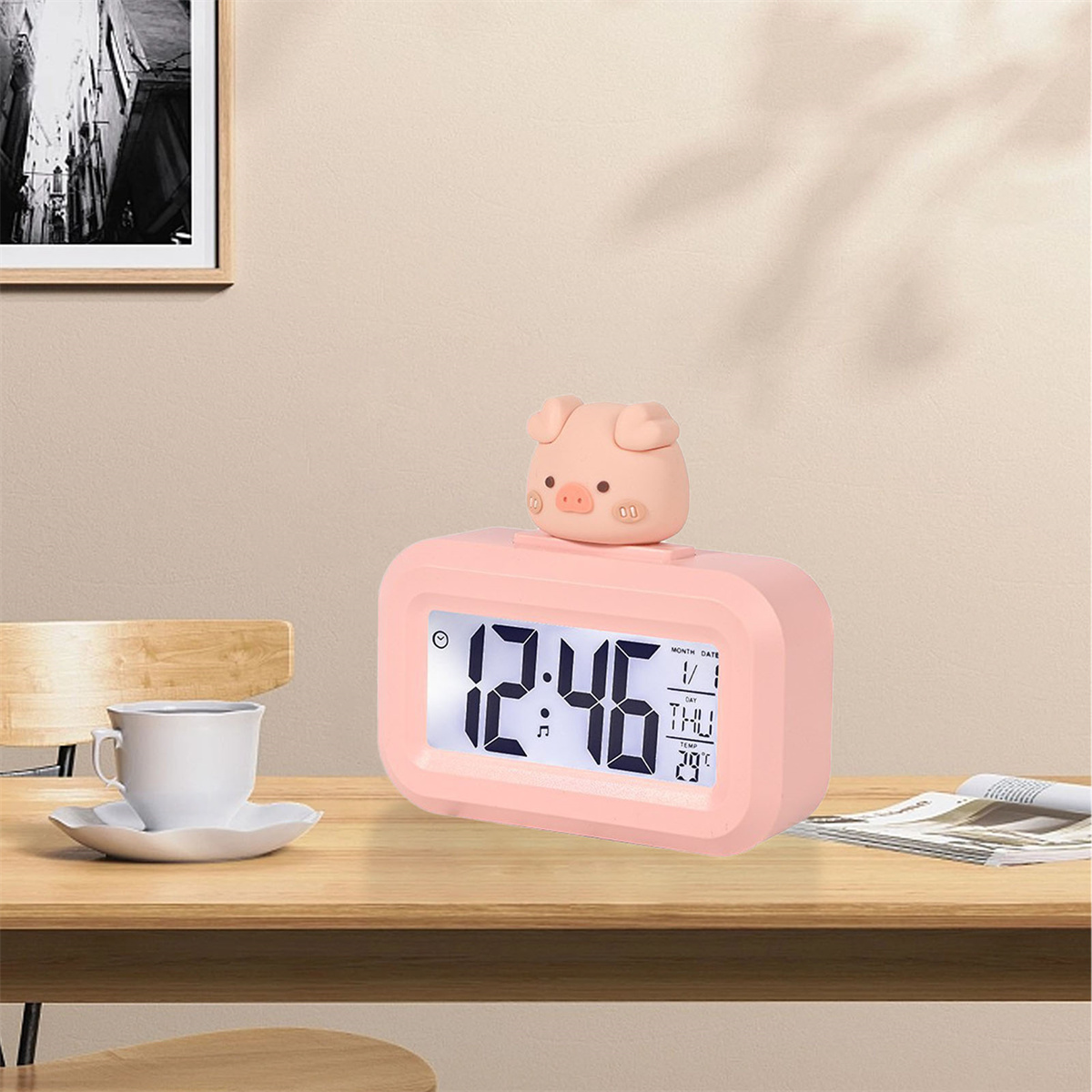 Rosa schwein-förmiger Wecker auf einem Tisch. Kaffeetasse und Kunst im Hintergrund.