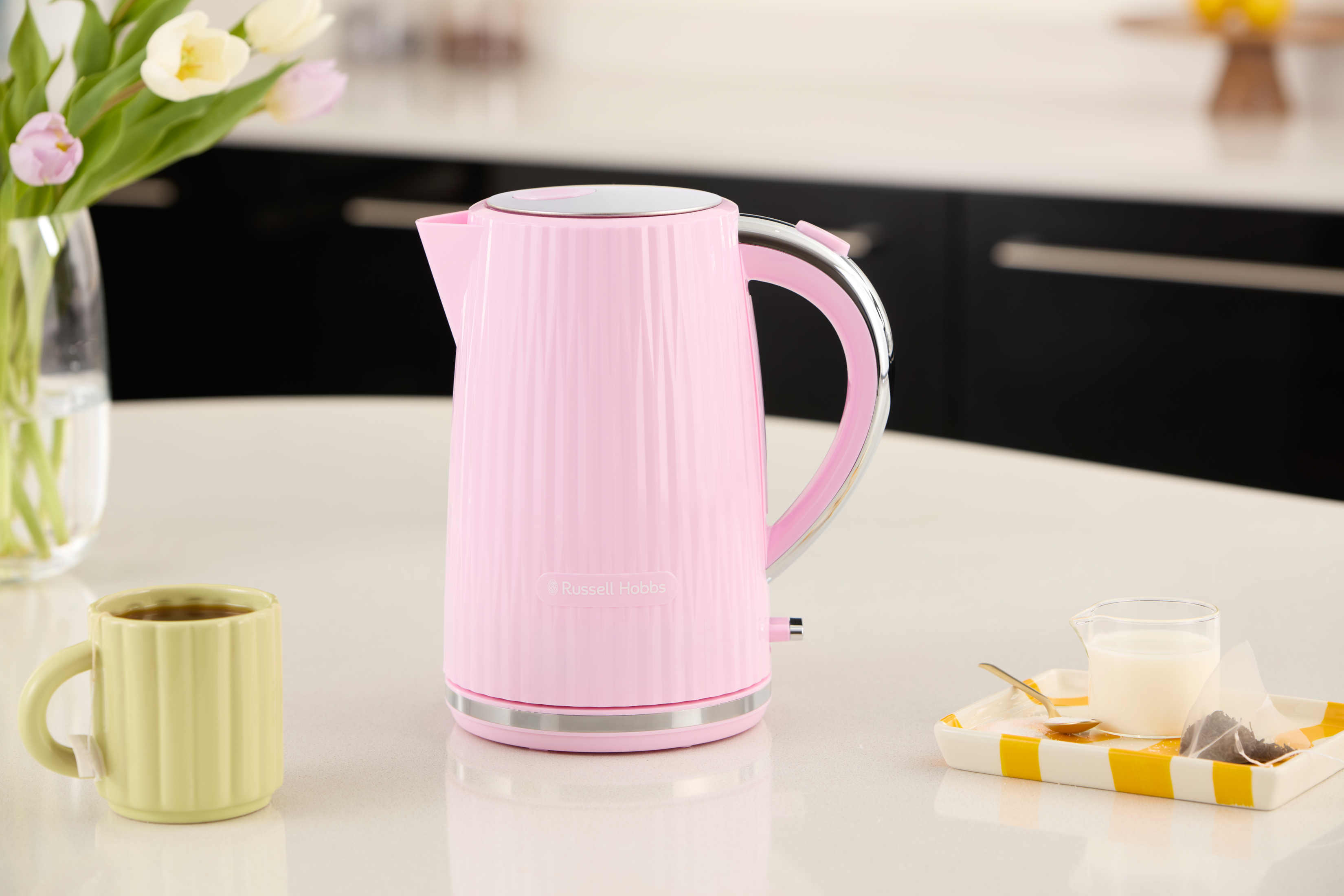 Bollitore rosa Russell Hobbs, una tazza di tè e un vassoio con latte e bustina di tè.
