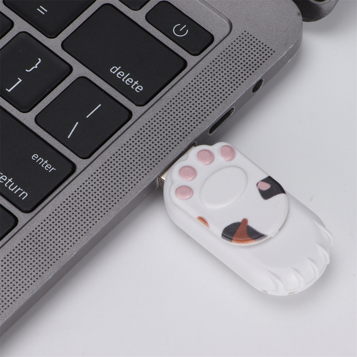 Ein weißer USB-Stick in Pfotenform, der an die Tastatur eines Laptops angeschlossen ist. Die Tastatur ist grau.