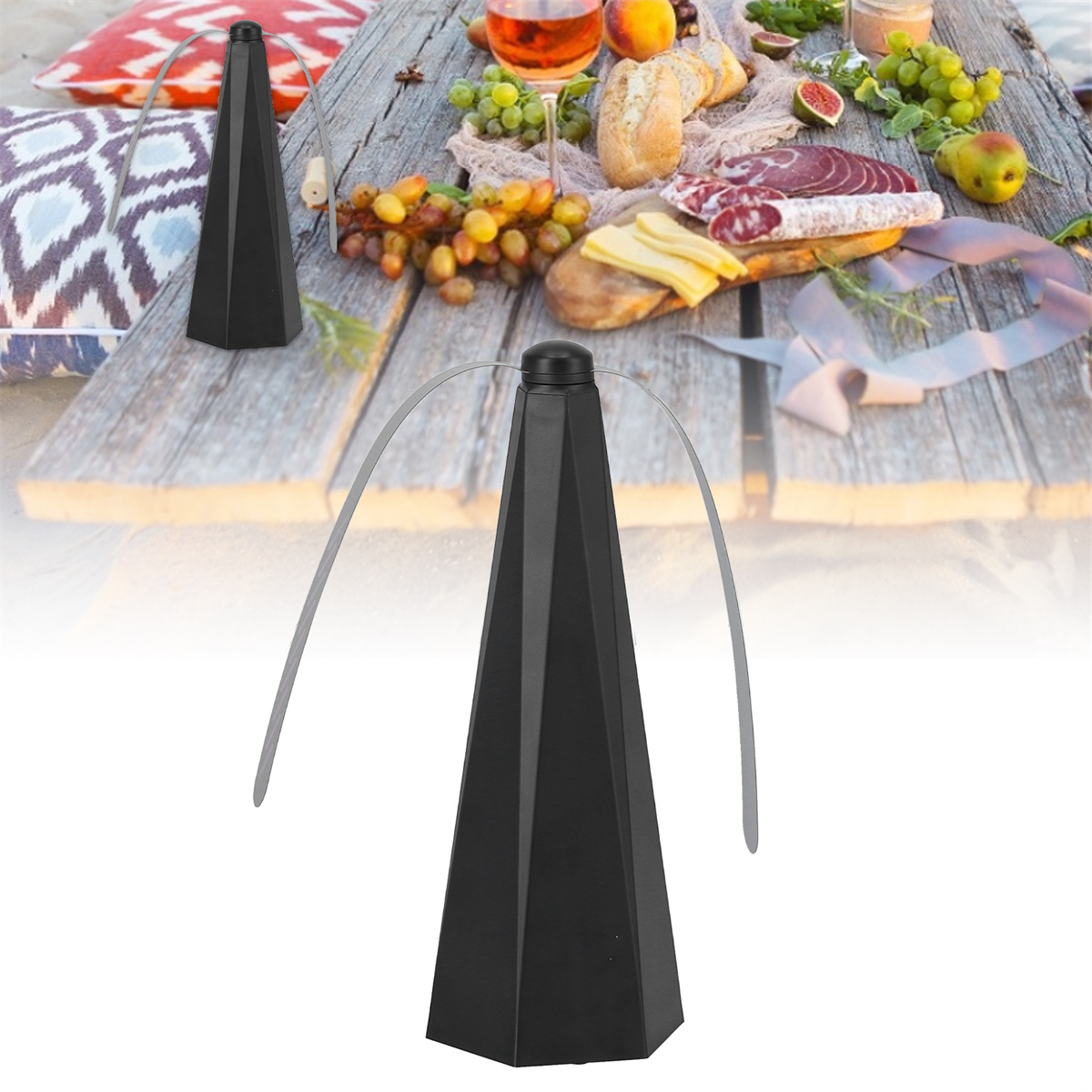 Ein schwarzer Ventilator auf einem Tisch, der für ein Picknick gedeckt ist. Es gibt Essen wie Trauben, Brot und ein Glas Wein.