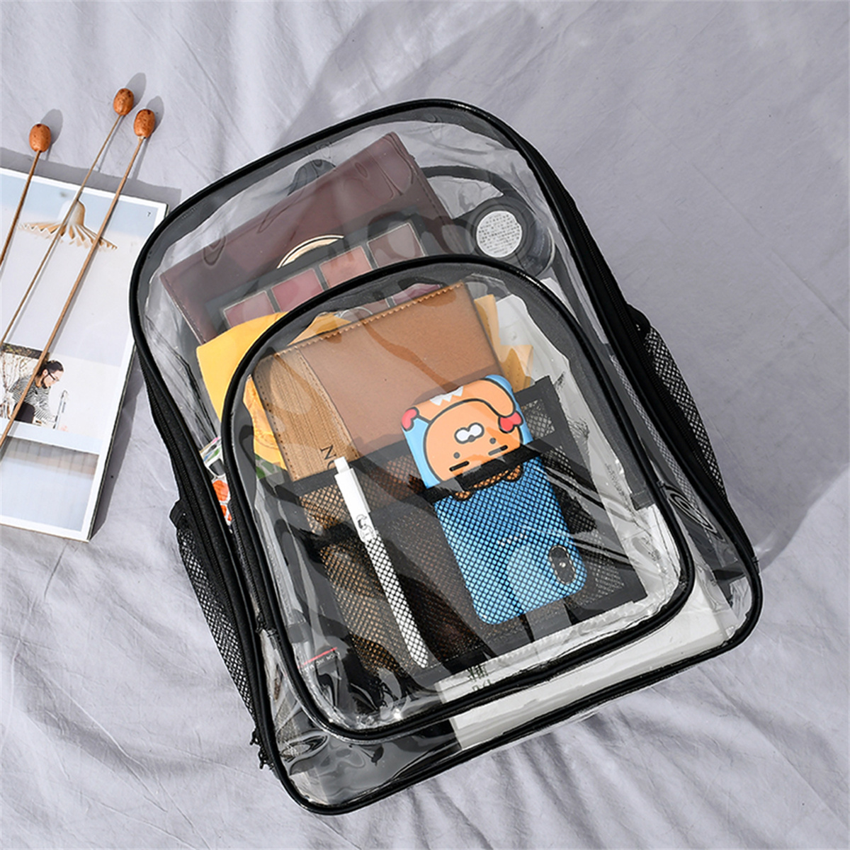 Ein durchsichtiger Rucksack mit Gegenständen darin: Geldbörse, Make-up, Portemonnaie.