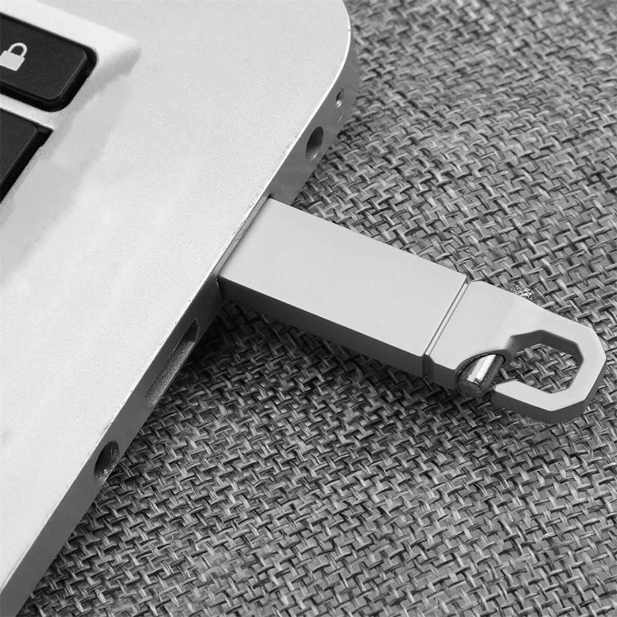 Ein USB-Stick, der in einen Laptop eingesteckt ist. Der Stick ist silberfarben und hat eine Schlaufe. Es ist auf grauer Oberfläche.