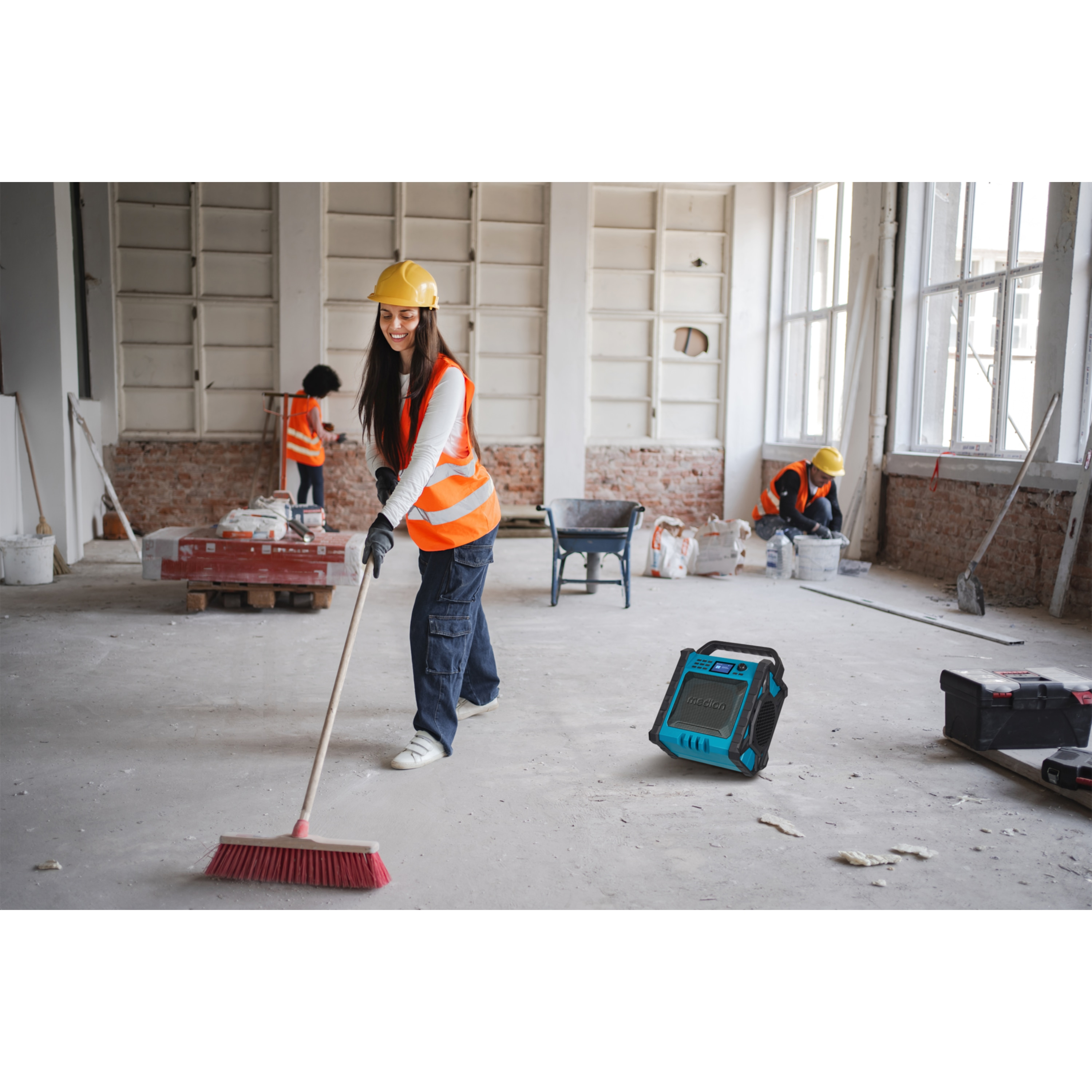 Ouvriers du bâtiment sur un chantier, un balayant, un autre utilisant la radio.