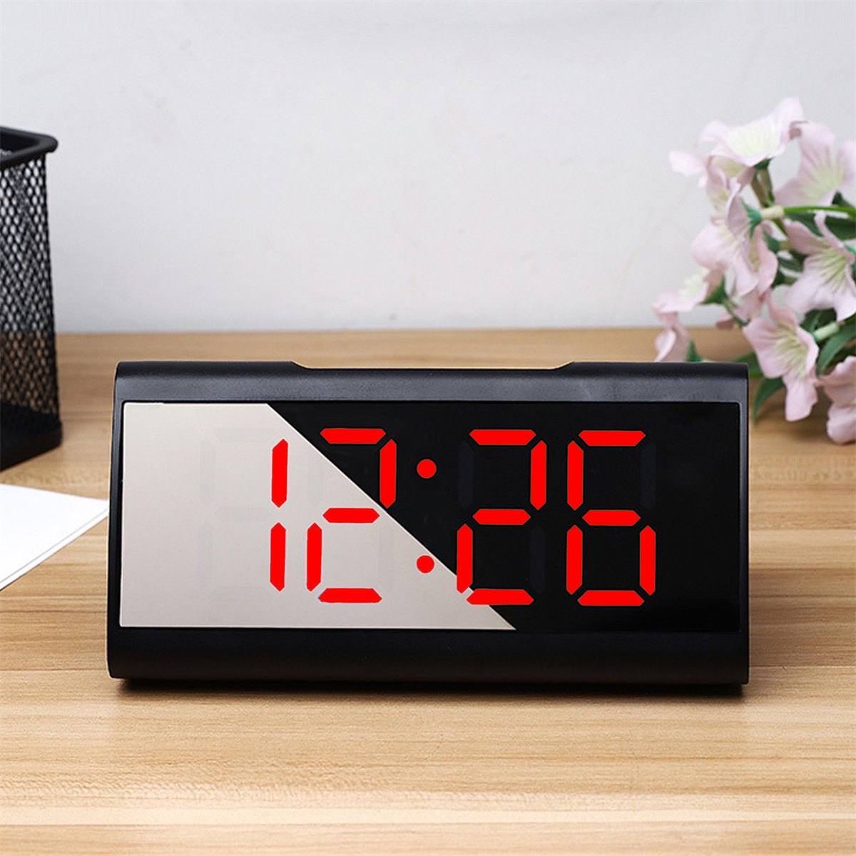 Schwarzer digitaler Wecker mit roter Anzeige 12:26 auf Holzoberfläche.