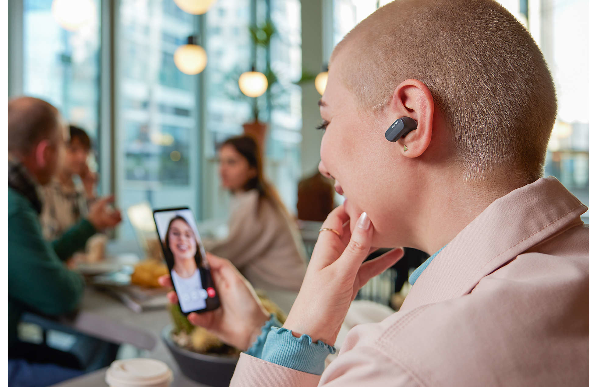 Mujer usando auriculares, mirando el teléfono que muestra videollamada con otras personas.