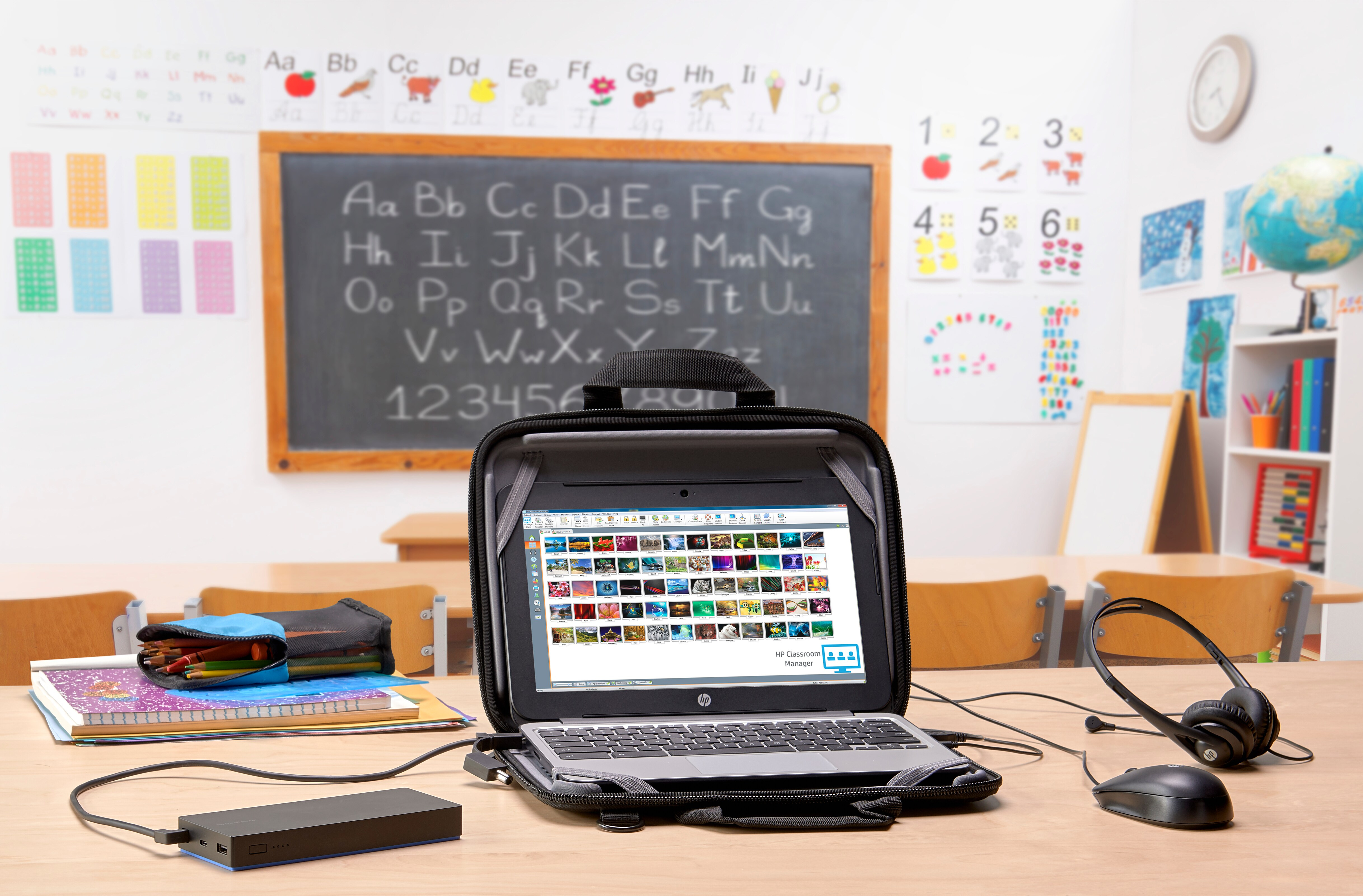 Laptop w klasie. Widoczna tablica, biurka i inne materiały szkolne.